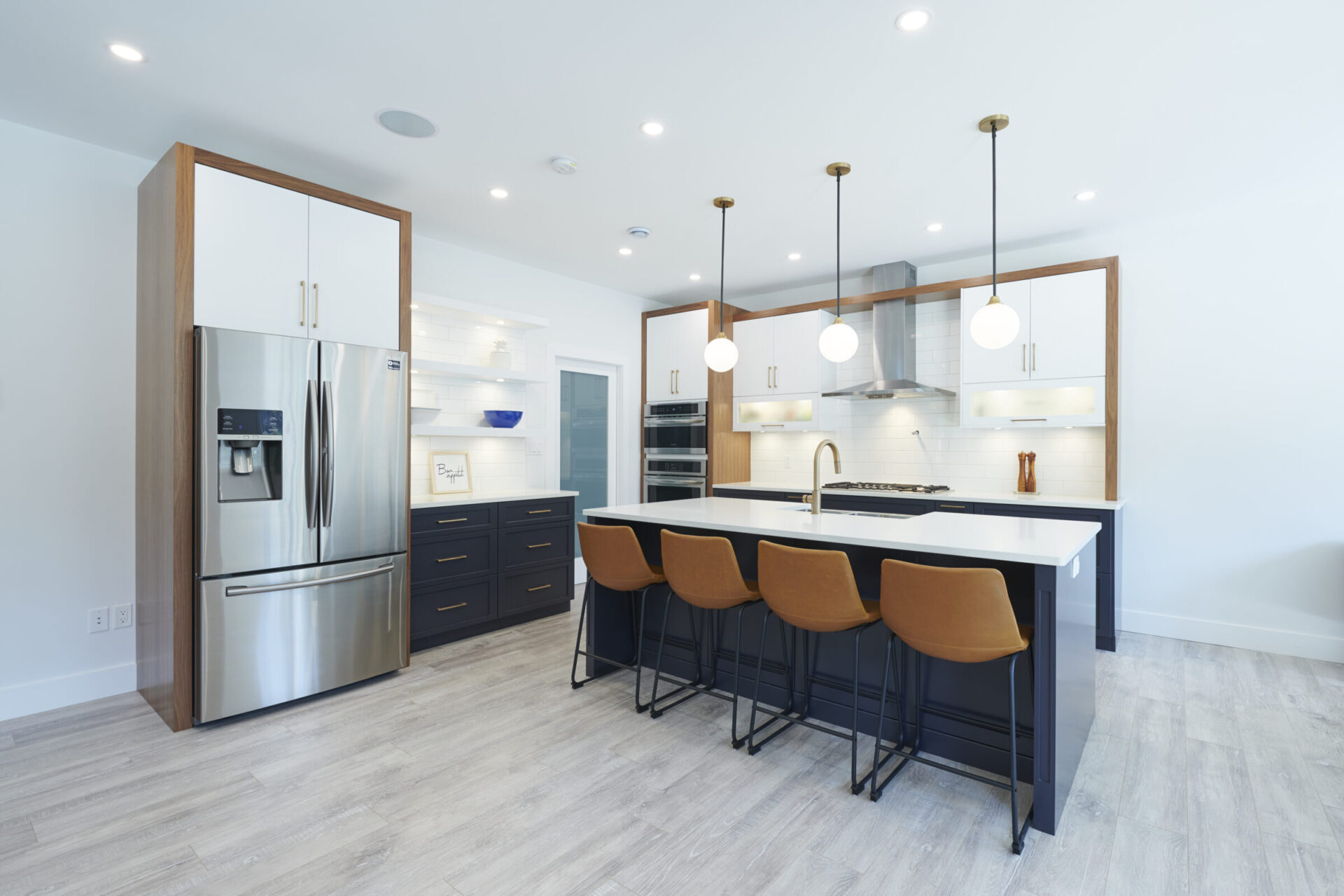A modern kitchen with stainless steel appliances, white countertops, dark cabinets, and a central island with brown stools under pendant lights.