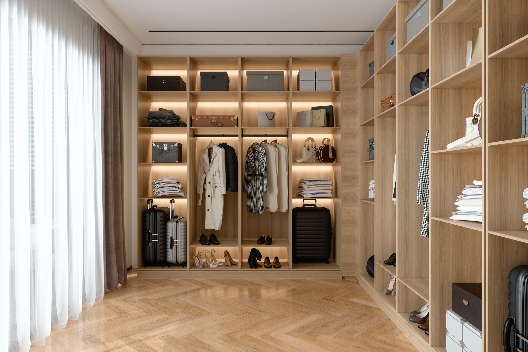 A well-organized, spacious walk-in closet with wooden shelves, neatly displayed clothes, shoes, bags, and suitcases, under soft lighting by a window.