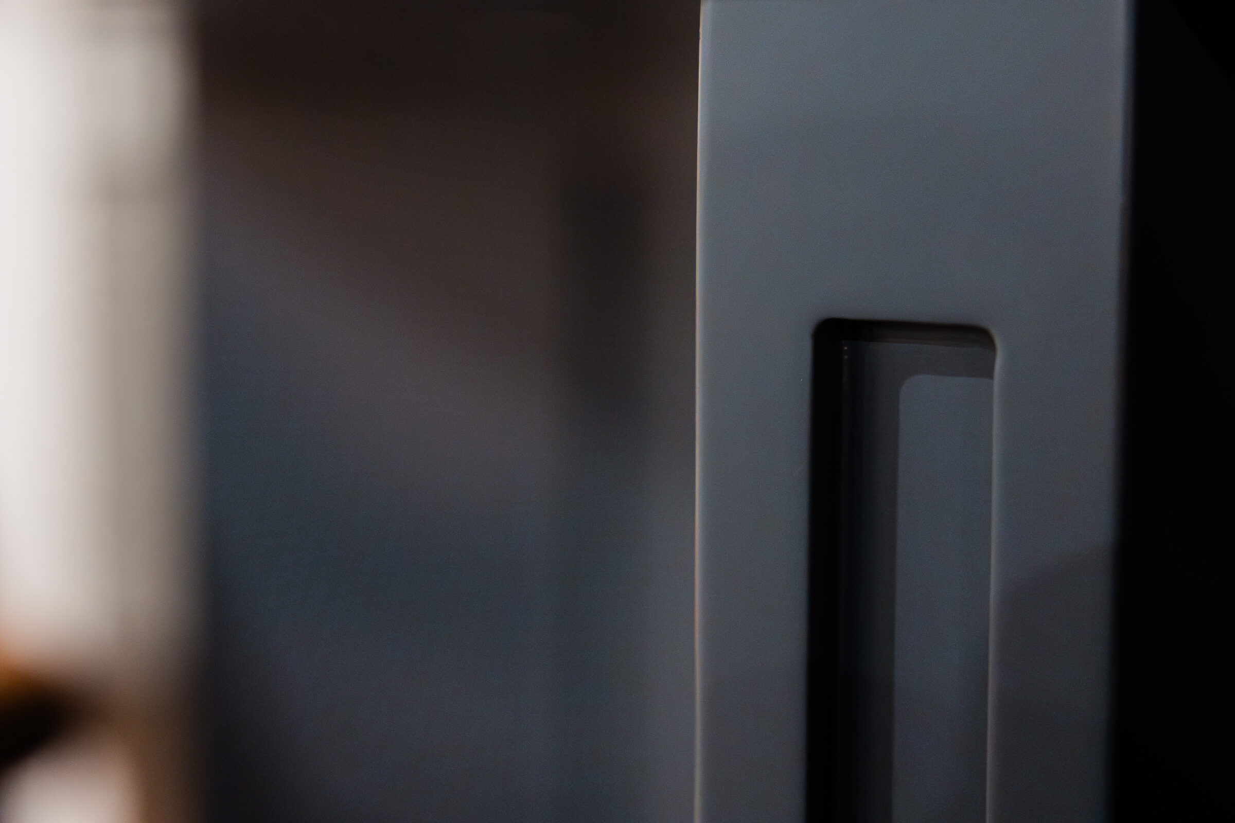 An abstract close-up of a modern, sleek device or structure with a blurred background, featuring gradients of black and grey tones with a reflective edge.