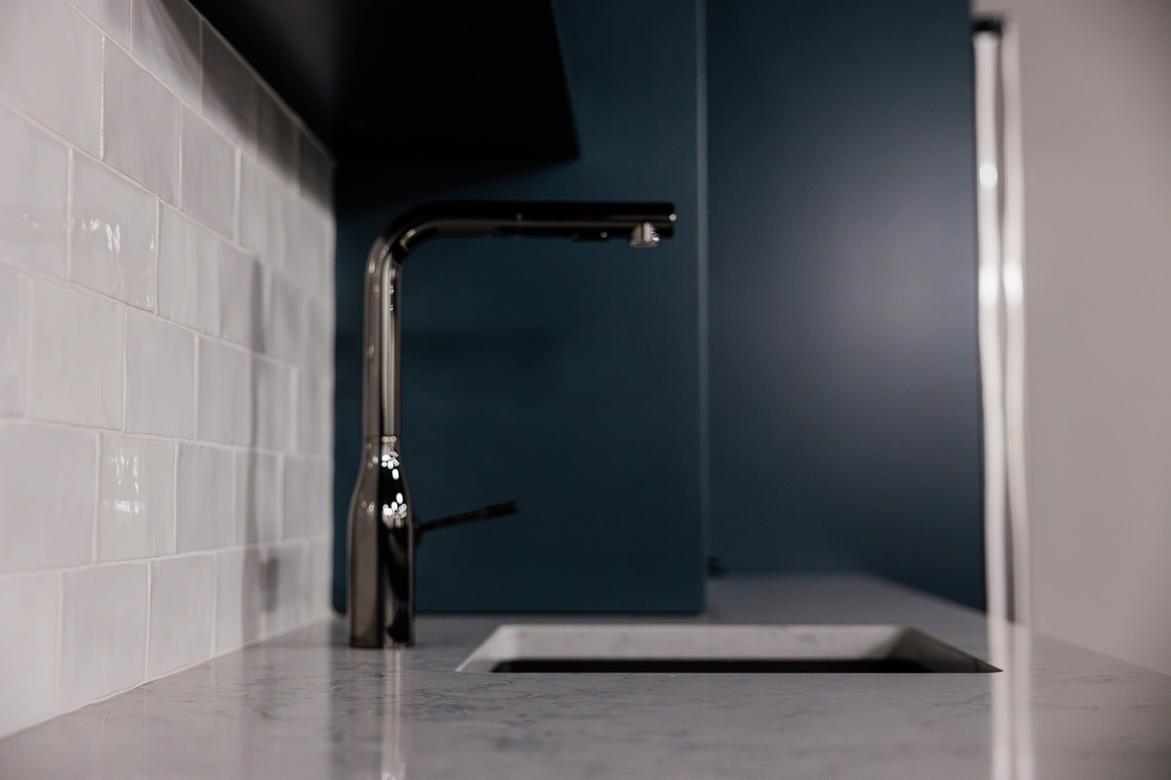 A modern kitchen sink with a stainless steel faucet against a blue wall and white subway tile backsplash, showcasing sleek and clean design elements.