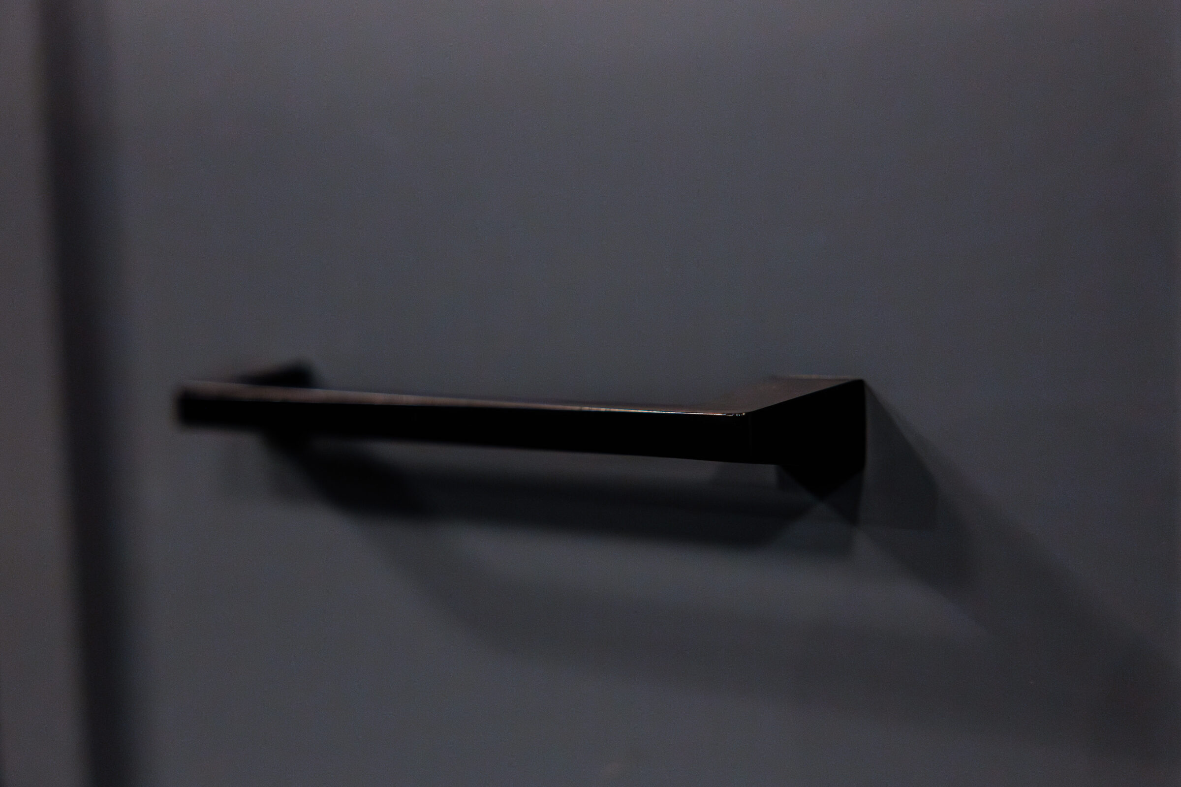 A simple, modern black shelf mounted on a dark wall, casting a soft shadow, is depicted in a minimalist, dimly lit environment.