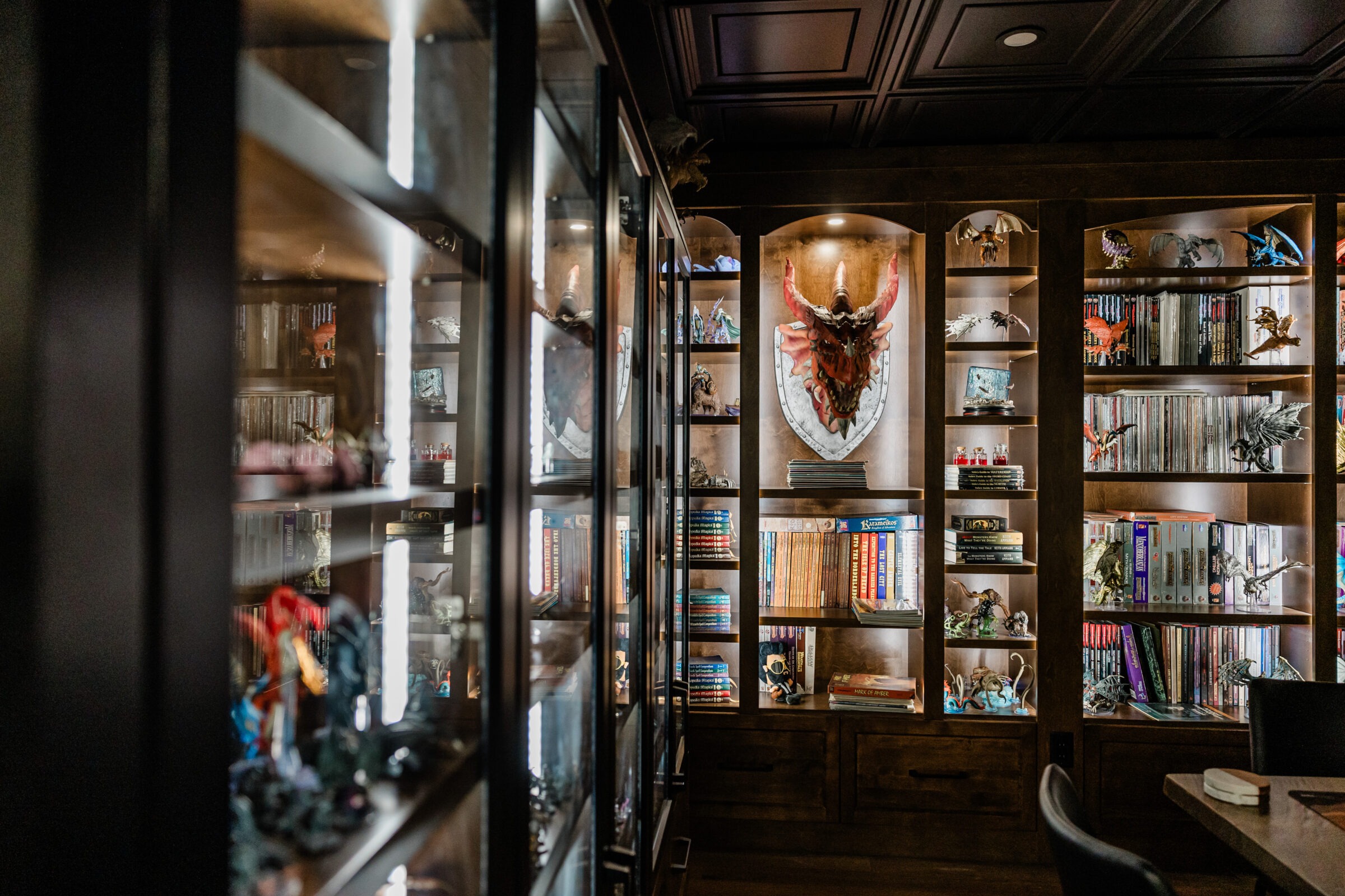 An elegant room with dark wooden shelves stocked with books, collectibles, and a skull decoration on the wall. Glass cabinets display additional items.