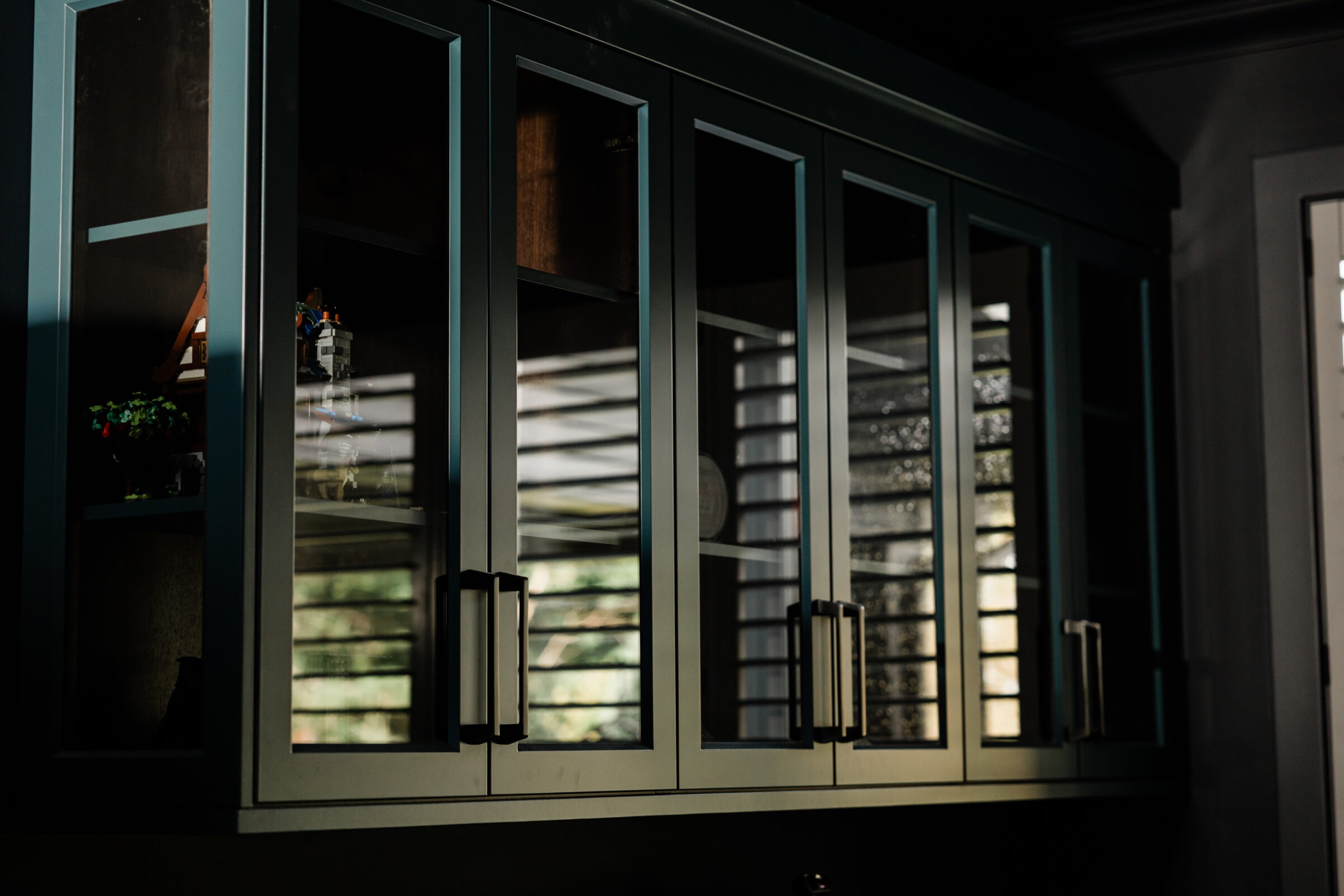 A row of dark wooden cabinets with glass doors, subtly reflecting a window, illuminated by natural light, creating a calm and serene atmosphere.
