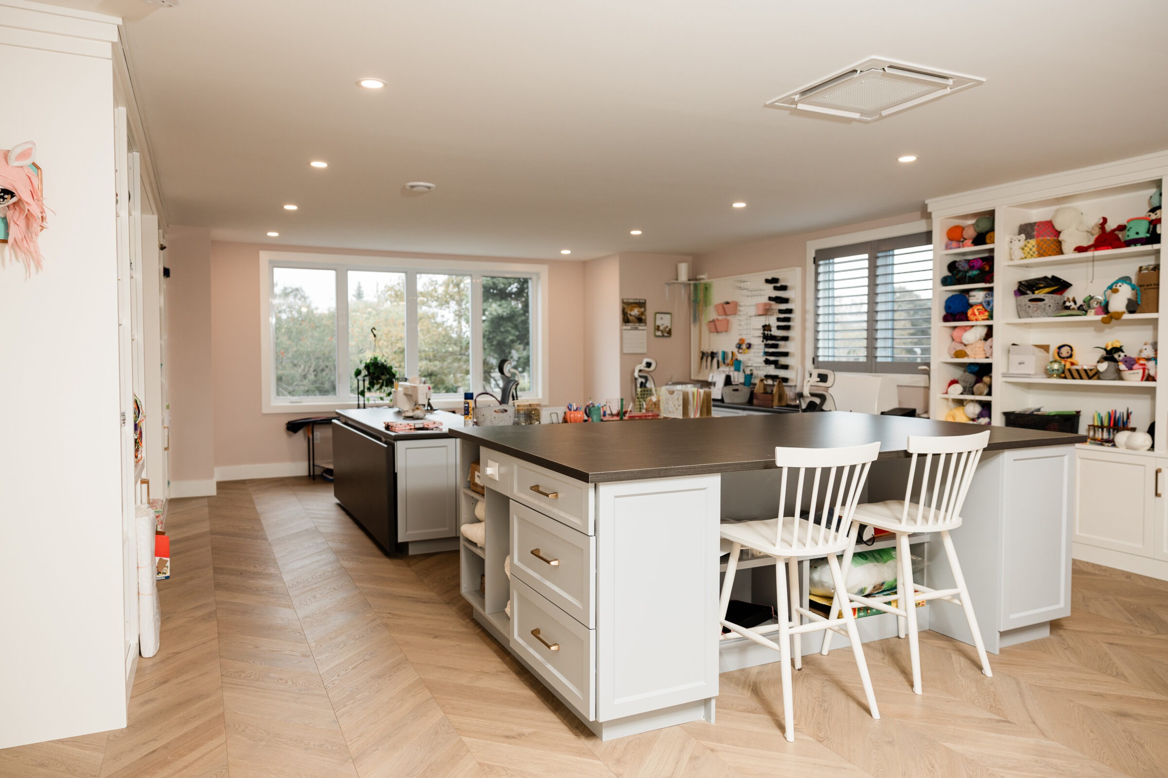 A spacious, well-lit kitchen with modern cabinetry, a central island with seating, and shelves filled with colorful yarns and crafts on the side.