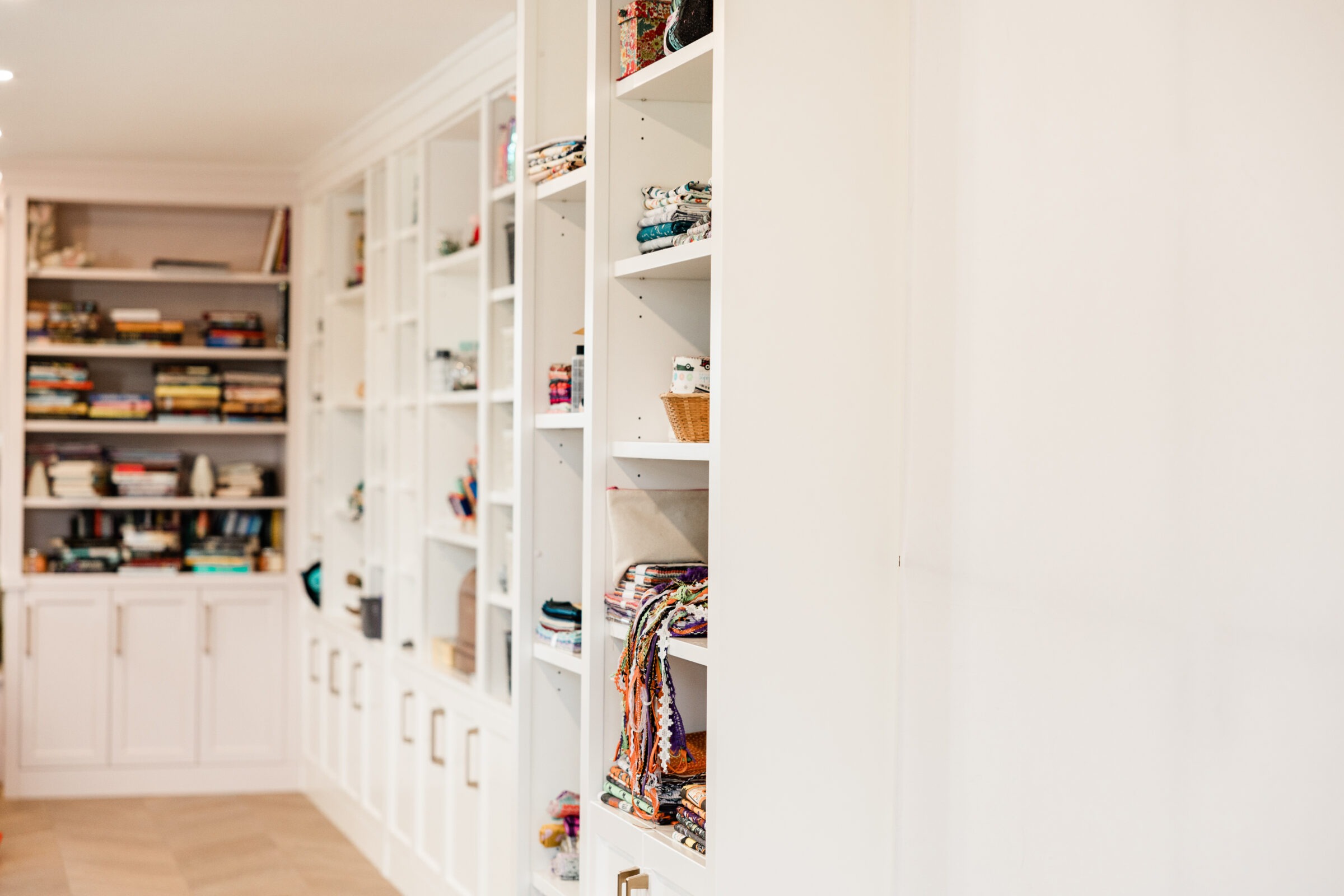 A spacious room with white built-in bookshelves lined with books, decorative items, woven baskets, and folded fabrics. The ambiance is bright and clean.
