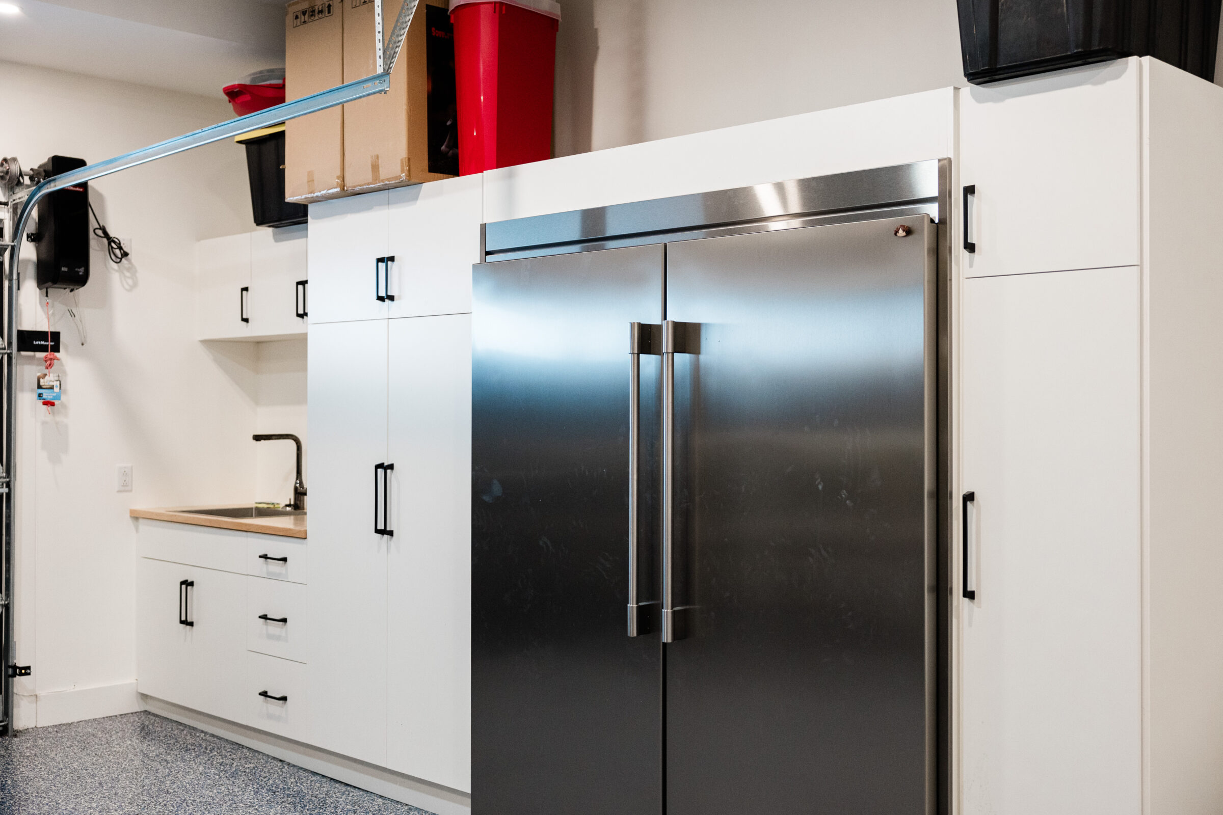 A modern kitchen with white cabinetry, a stainless steel double-door refrigerator, and a countertop with a sink. The floor is speckled and blue-gray.