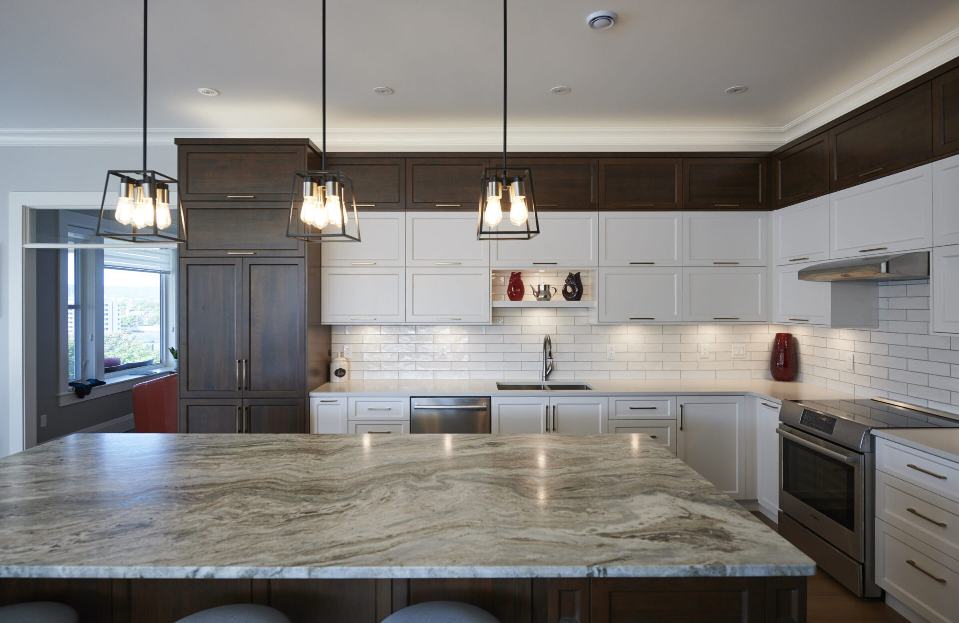 This is a modern kitchen with white cabinetry, stainless steel appliances, subway tile backsplash, dark wood accents, and contemporary hanging lights.