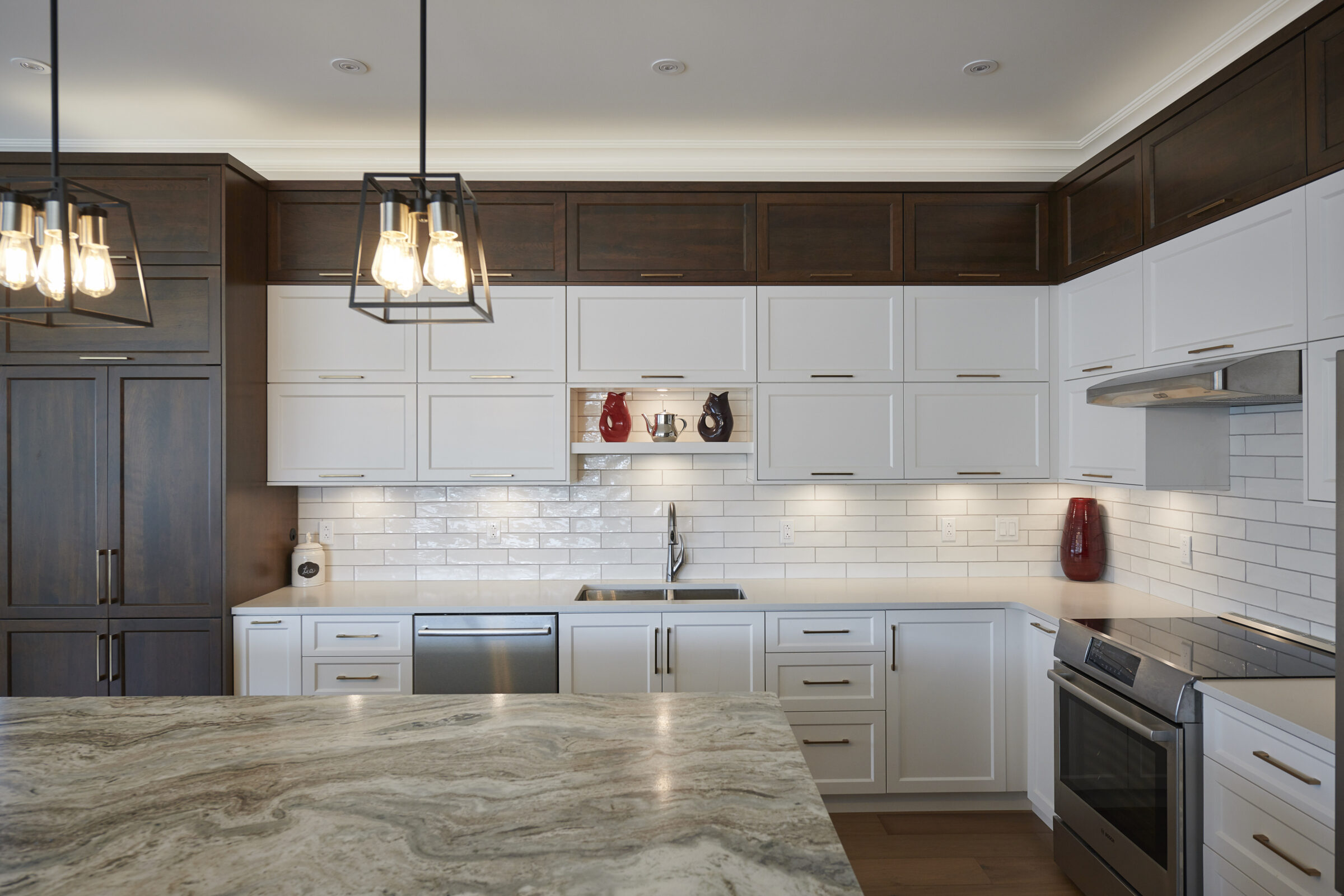 Modern kitchen interior with white and dark wood cabinets, subway tile backsplash, stainless steel appliances, and hanging pendant lights over an island.