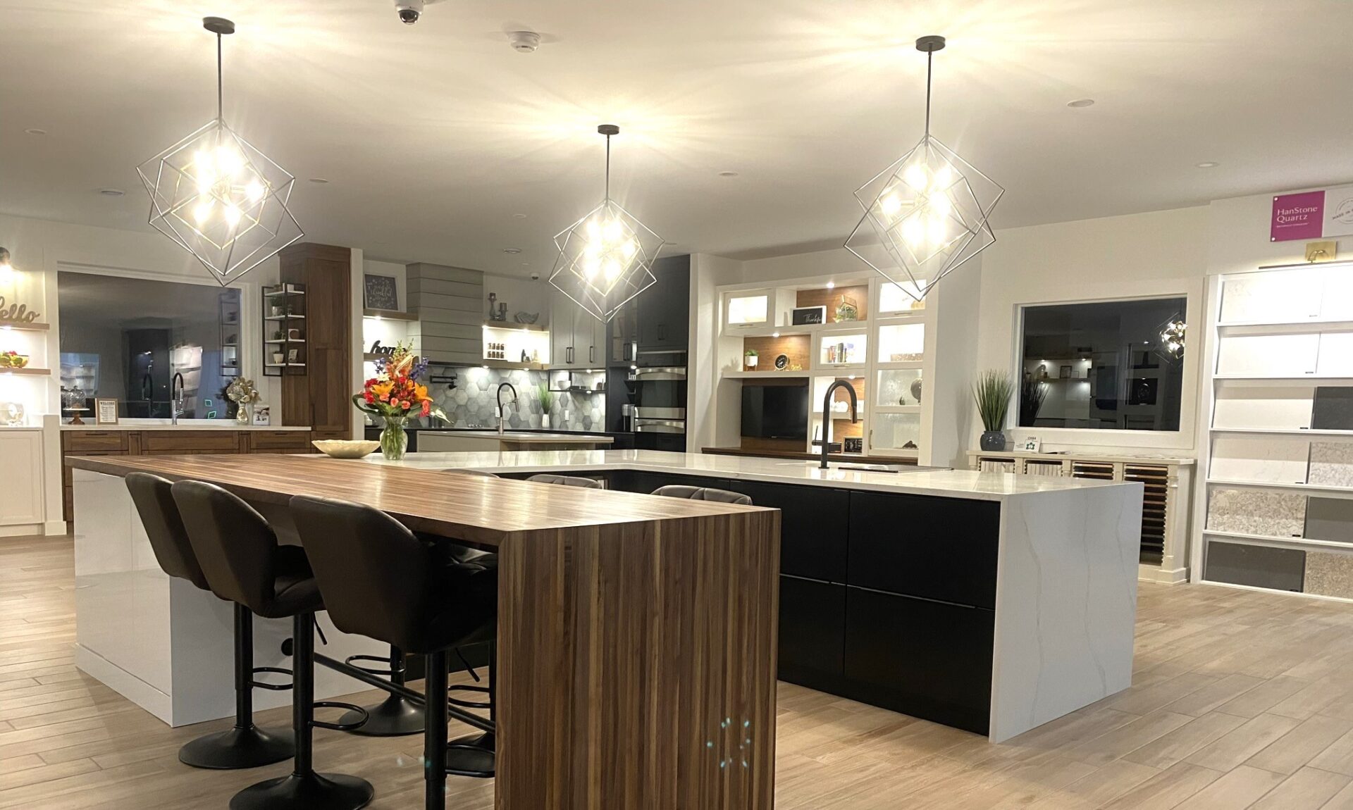 A modern kitchen with geometric pendant lights, a large island with seating, dark cabinetry, built-in appliances, and white countertops.