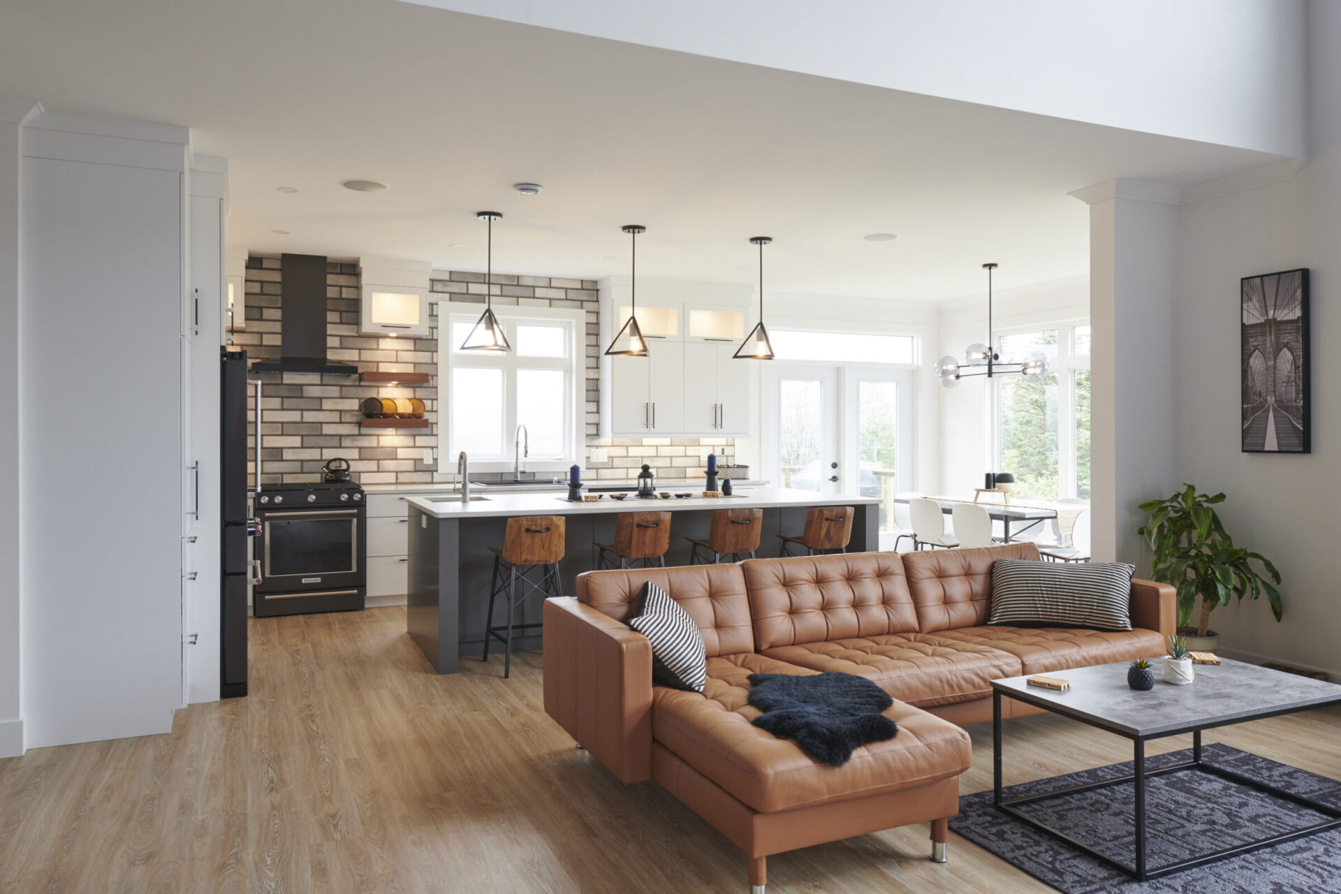 Modern open-plan living space with a kitchen area, leather couch, dining set, pendant lights, and a mix of natural and artificial lighting.