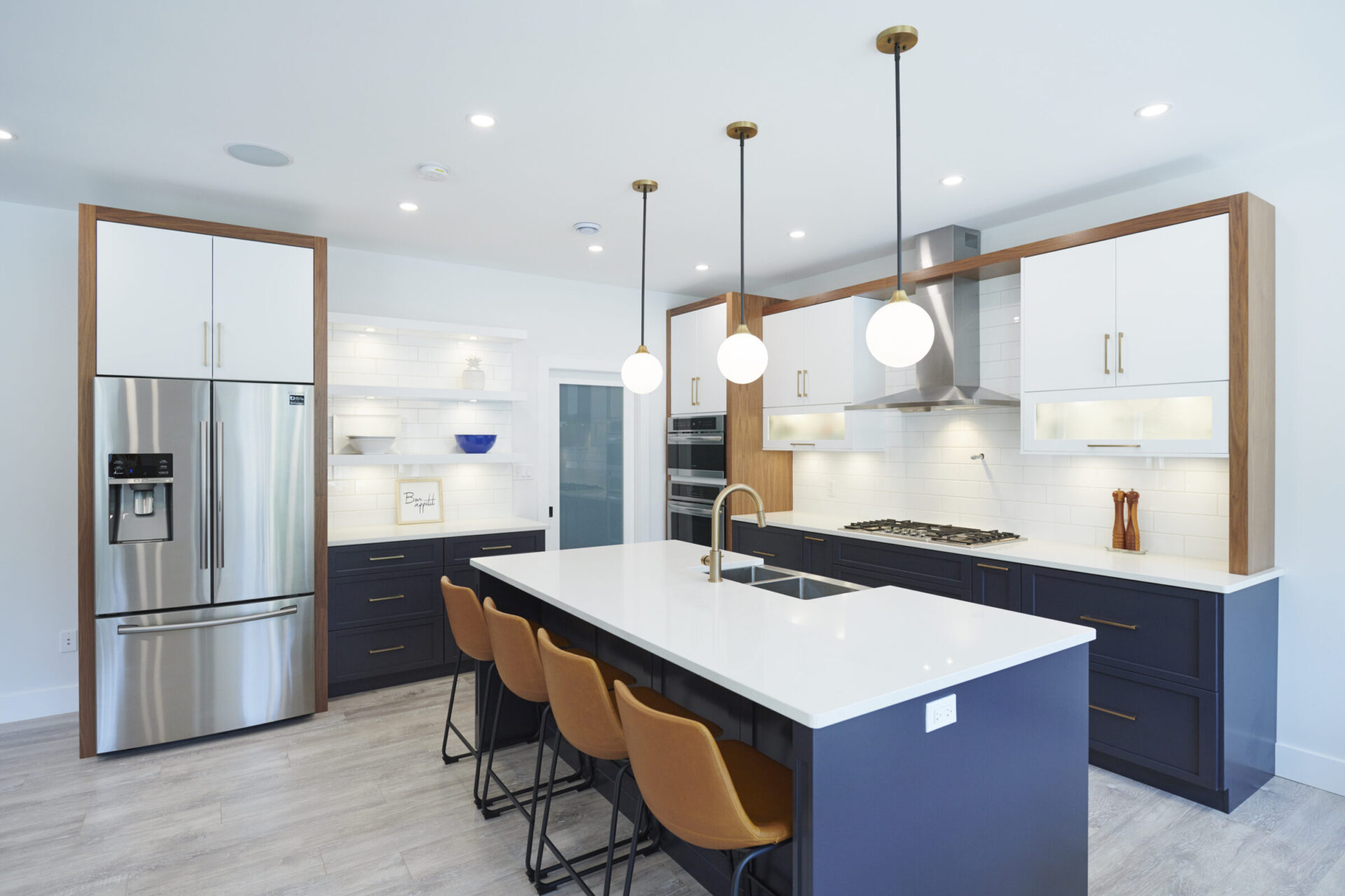 Modern kitchen interior with white walls, blue cabinets, stainless steel appliances, wooden accents, an island with brown chairs, and pendant lights.