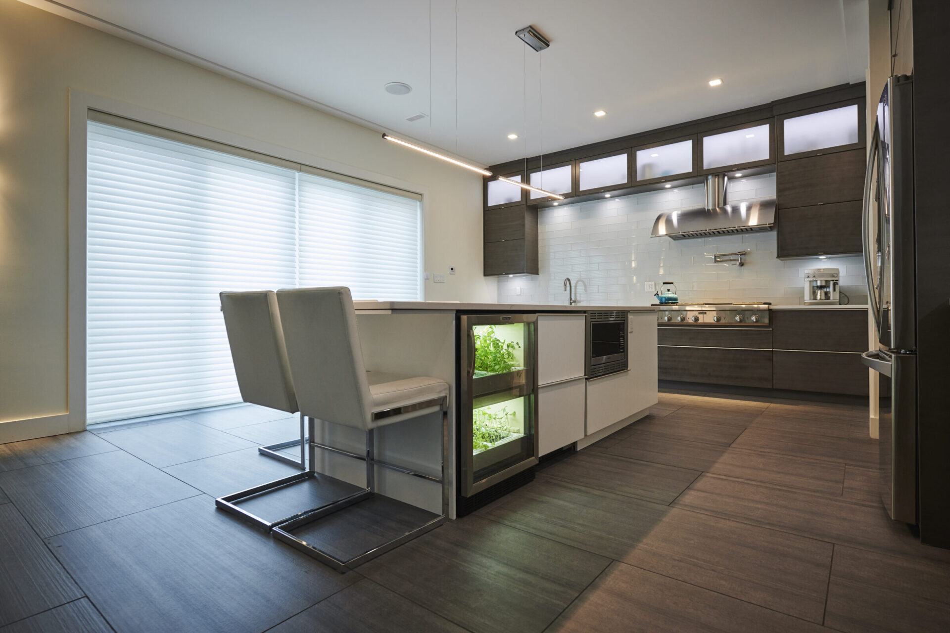 A modern kitchen with dark wooden floors, sleek cabinets, stainless steel appliances, a dining area, and an integrated indoor herb garden.