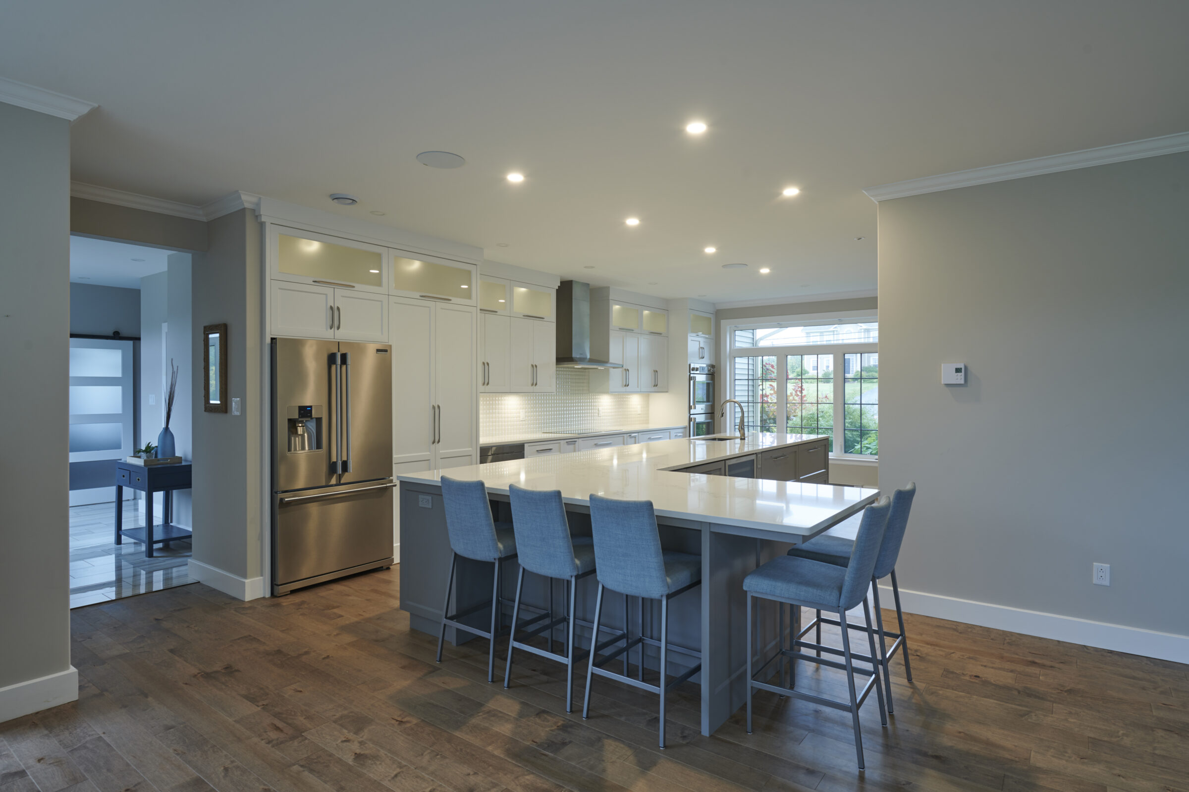 A modern kitchen with white cabinets, stainless steel appliances, hardwood floors, and a central island with blue bar stools. Bright, spacious, and contemporary design.