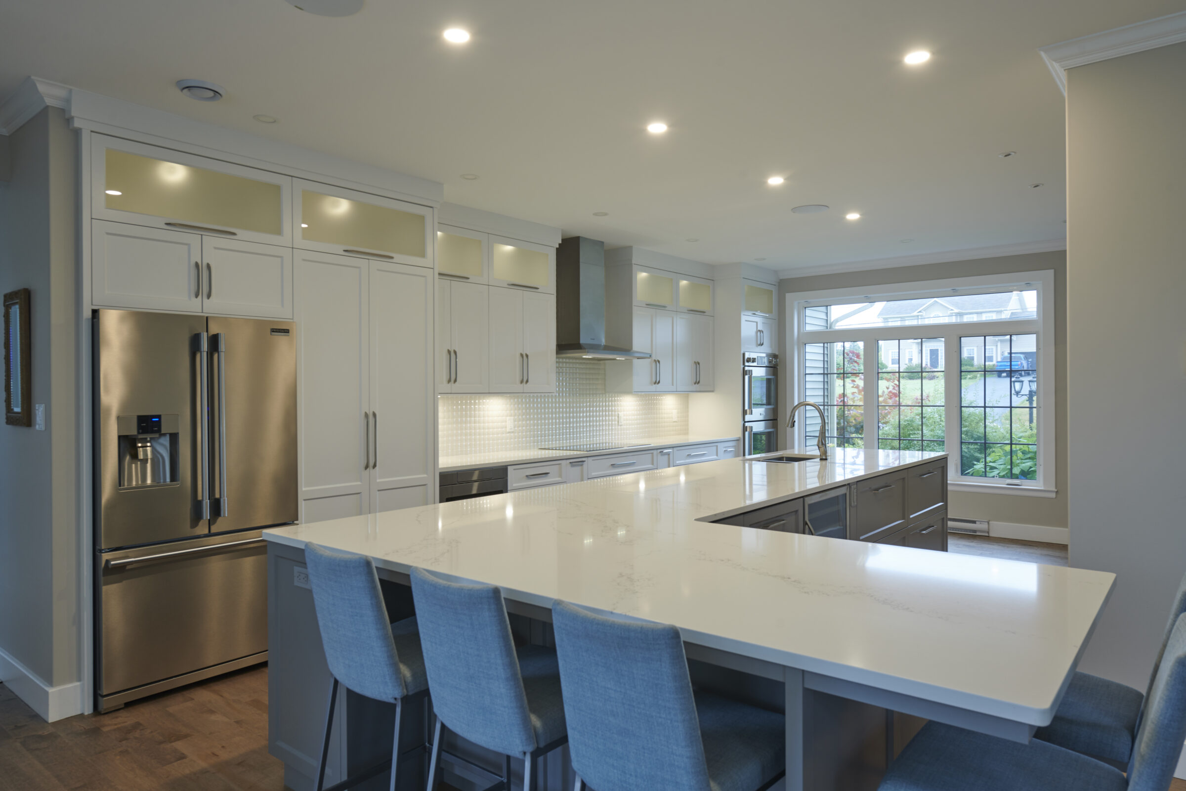 Modern kitchen with white cabinets, stainless steel appliances, large island with seating, pendant lights, and a view of the garden through a window.