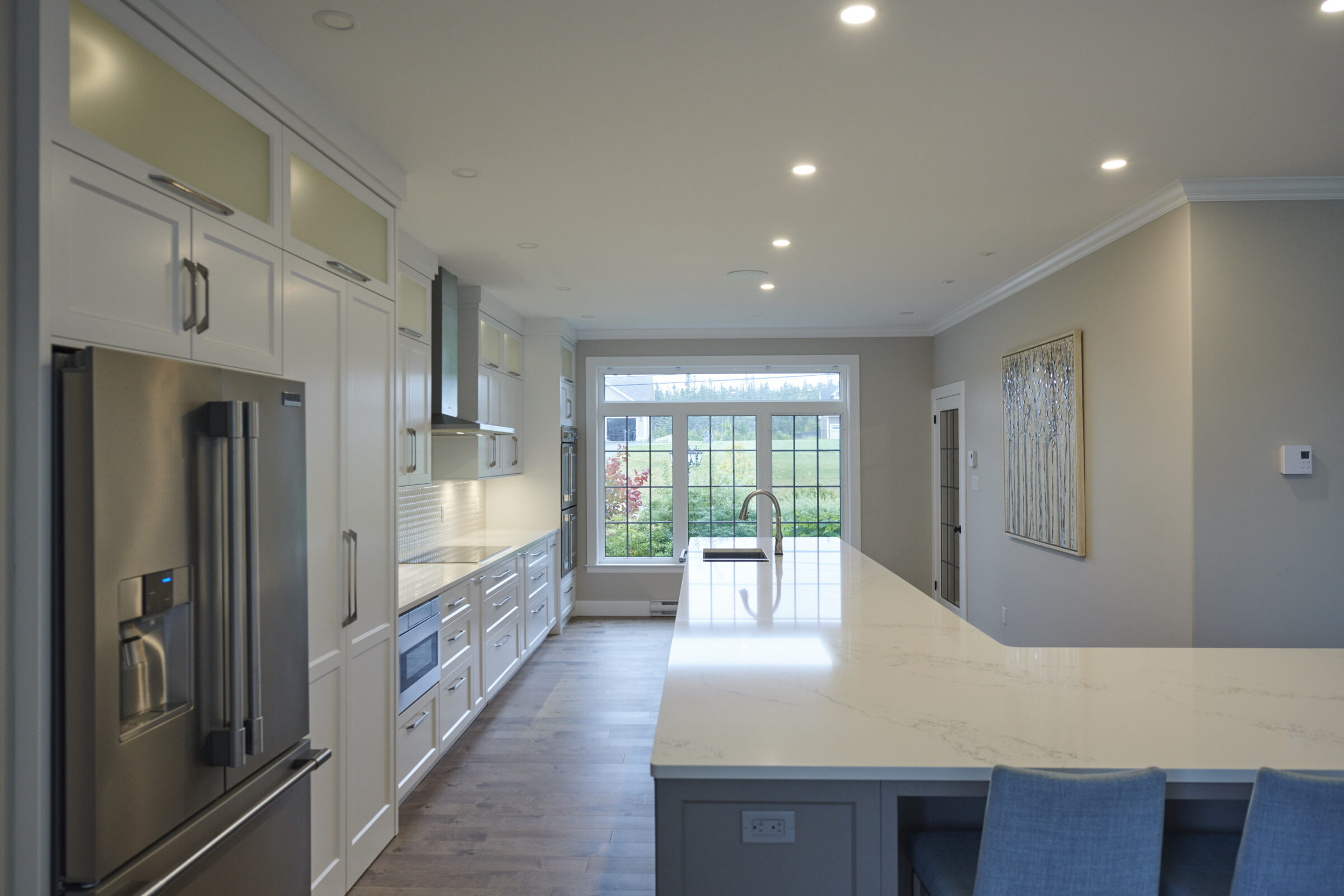 A modern kitchen with white cabinetry, stainless steel appliances, a central island with blue chairs, under-cabinet lighting, and recessed ceiling lights.