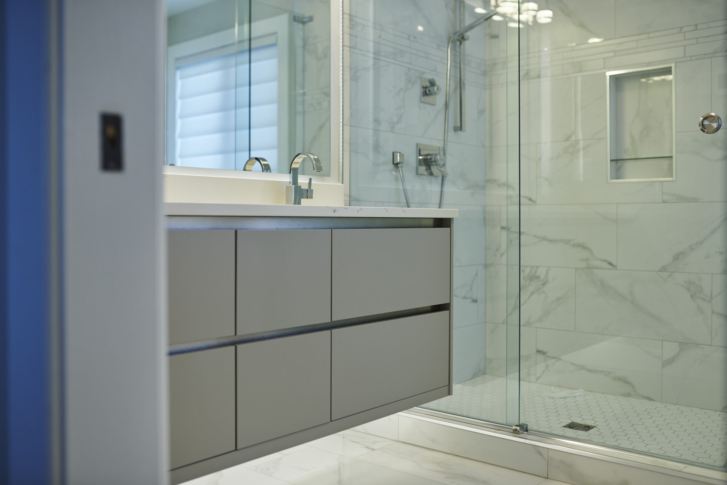 Modern bathroom interior with a marble vanity countertop, large mirror, and a glass-walled shower. Muted color scheme with natural light.