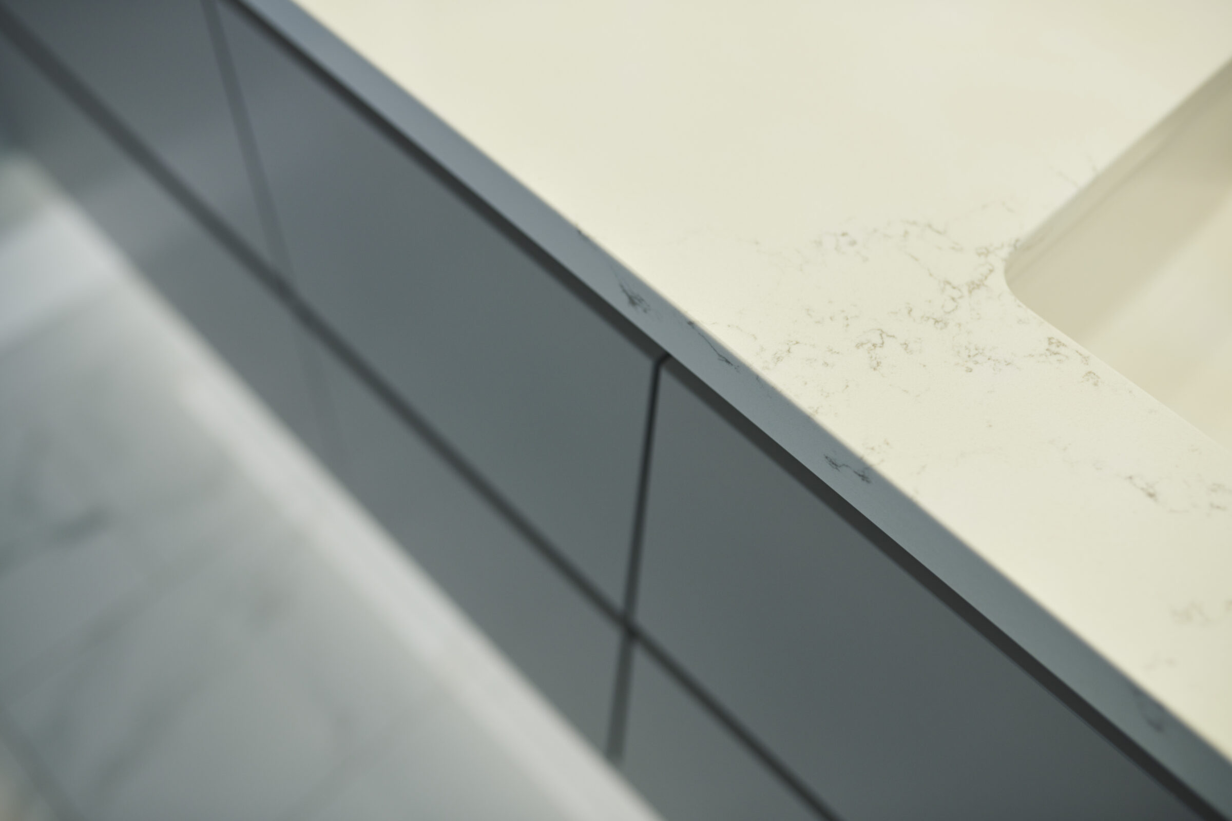 This image shows a close-up of a modern countertop with a marble-like surface, alongside sleek, grey cabinetry with minimalistic handles.