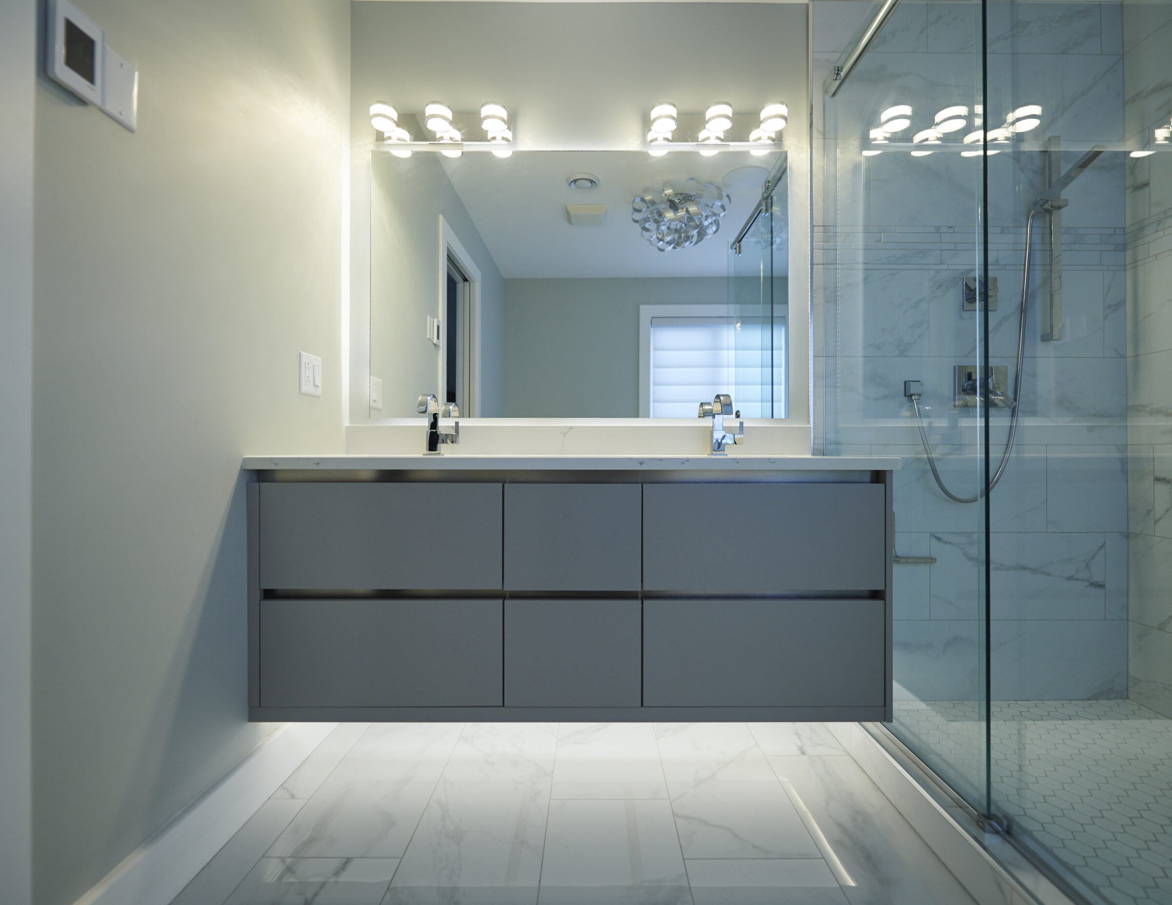 A modern bathroom with marble tiles, a floating double-sink vanity, large mirror, and a glass-enclosed shower with multiple showerheads and lighting above.