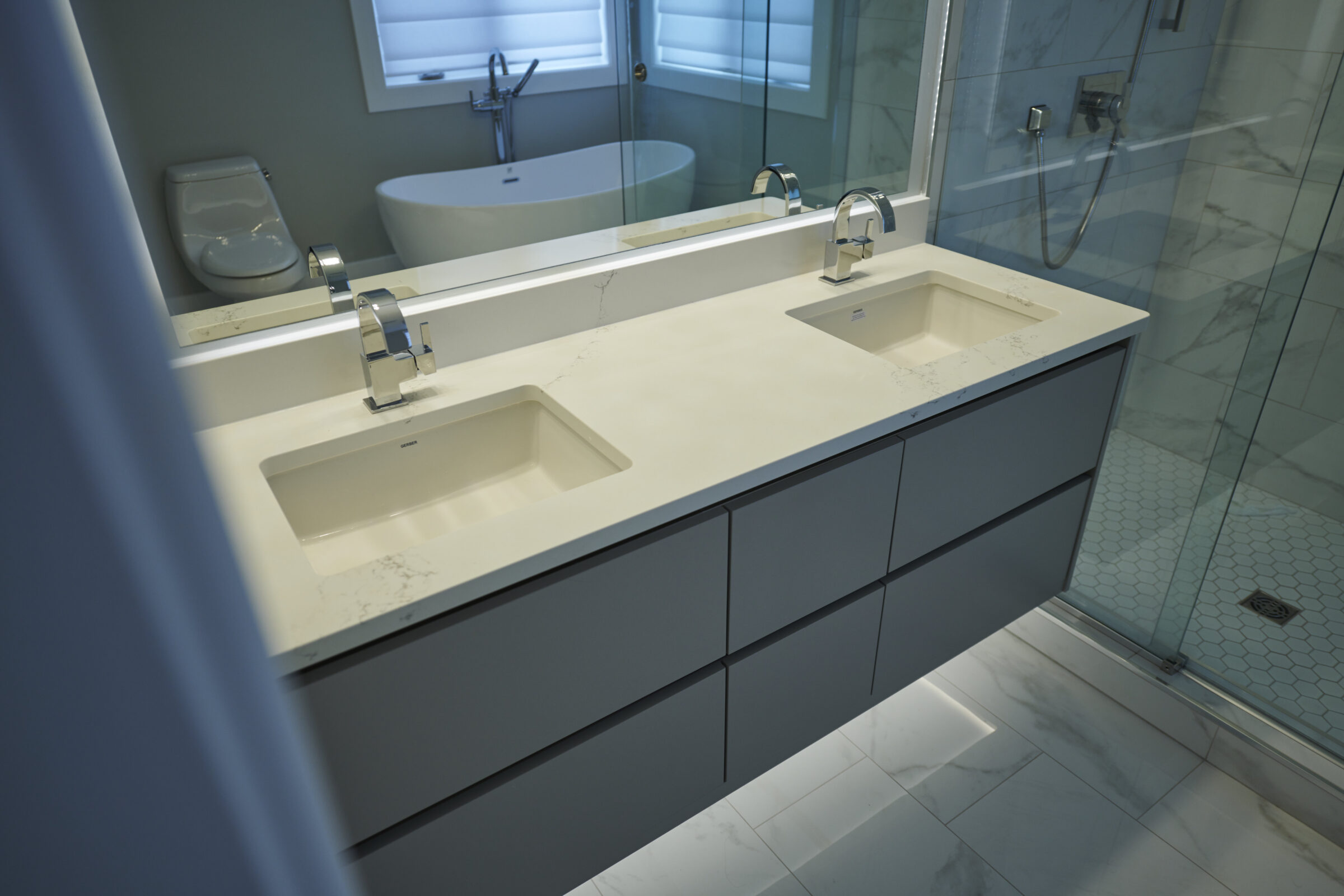 A modern bathroom featuring a double vanity with rectangular sinks, chrome faucets, large mirror, and a glass-enclosed shower with hexagonal tile flooring.