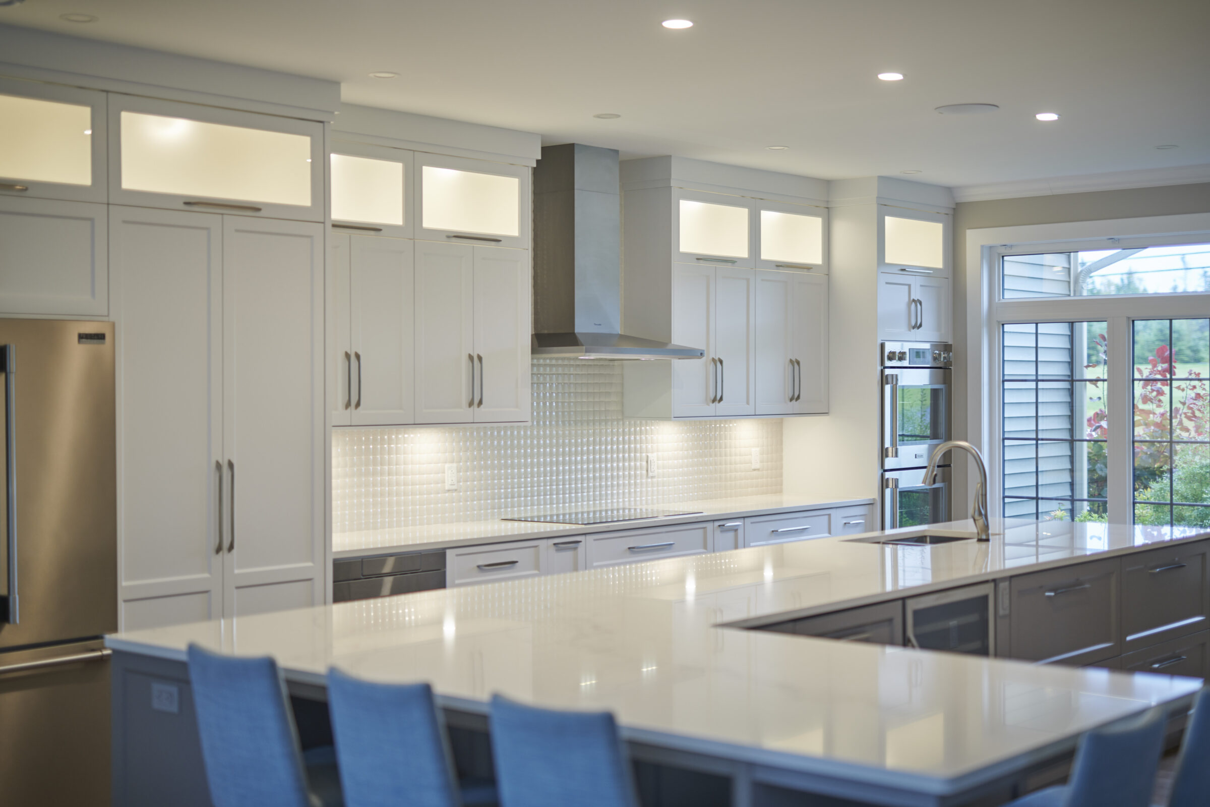 Modern kitchen interior with white cabinetry, stainless steel appliances, a tiled backsplash, and a glossy countertop. Natural light streams through the patio door.