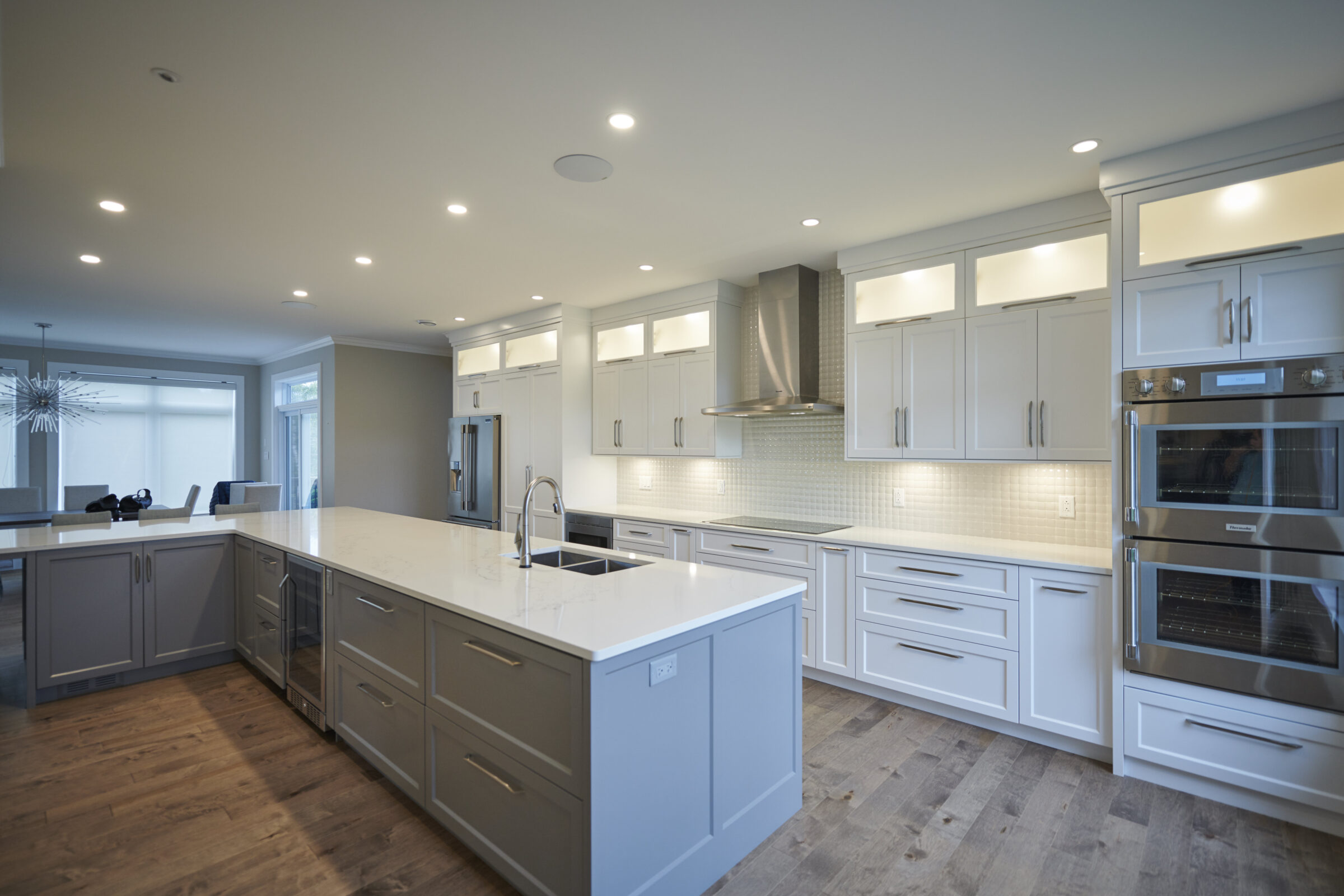 Modern kitchen with white cabinets, stainless steel appliances, a central island with a sink, and hardwood flooring under bright recessed lighting.