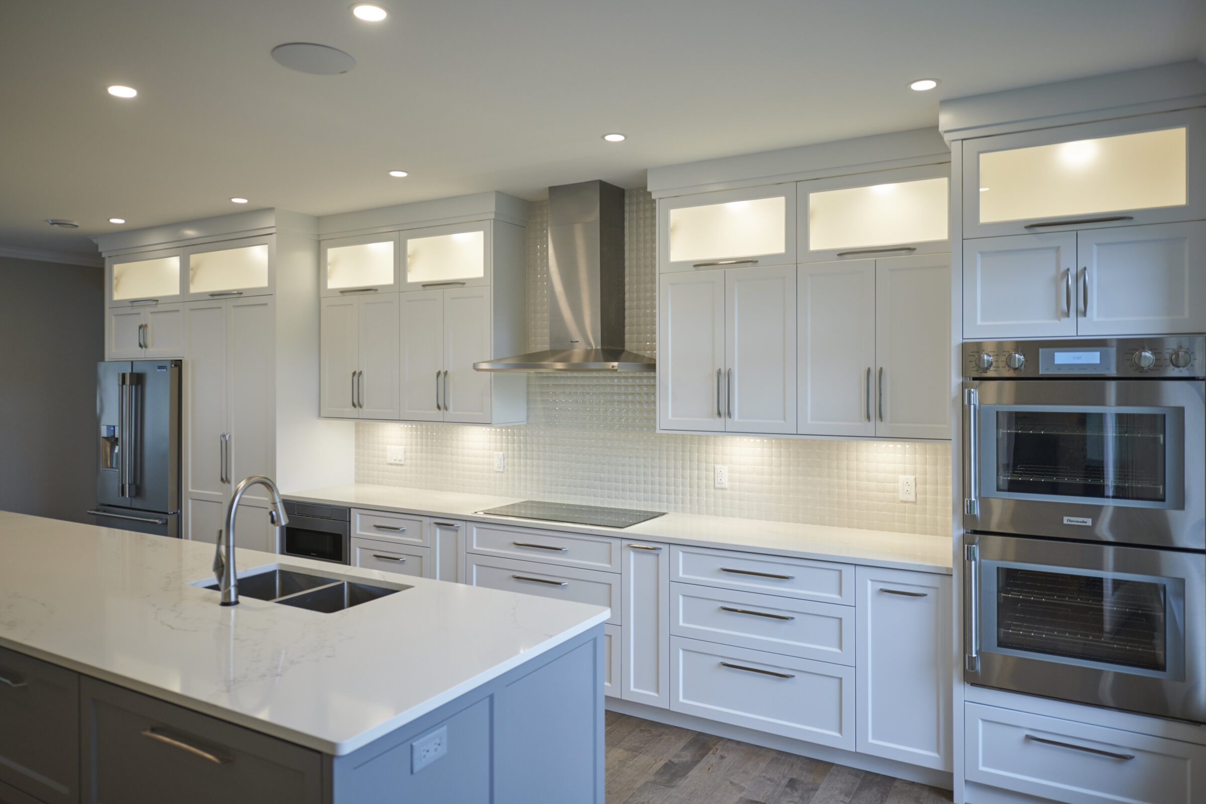 Modern kitchen with white cabinetry, stainless steel appliances, a central island, recessed lighting, and a tiled backsplash. The space is clean and bright.