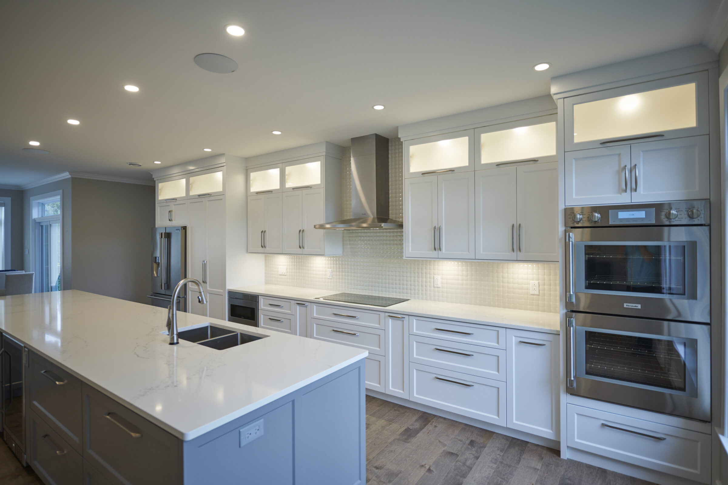 A modern kitchen with white cabinets, stainless steel appliances, recessed lighting, and a central island with a sink and a marble countertop.