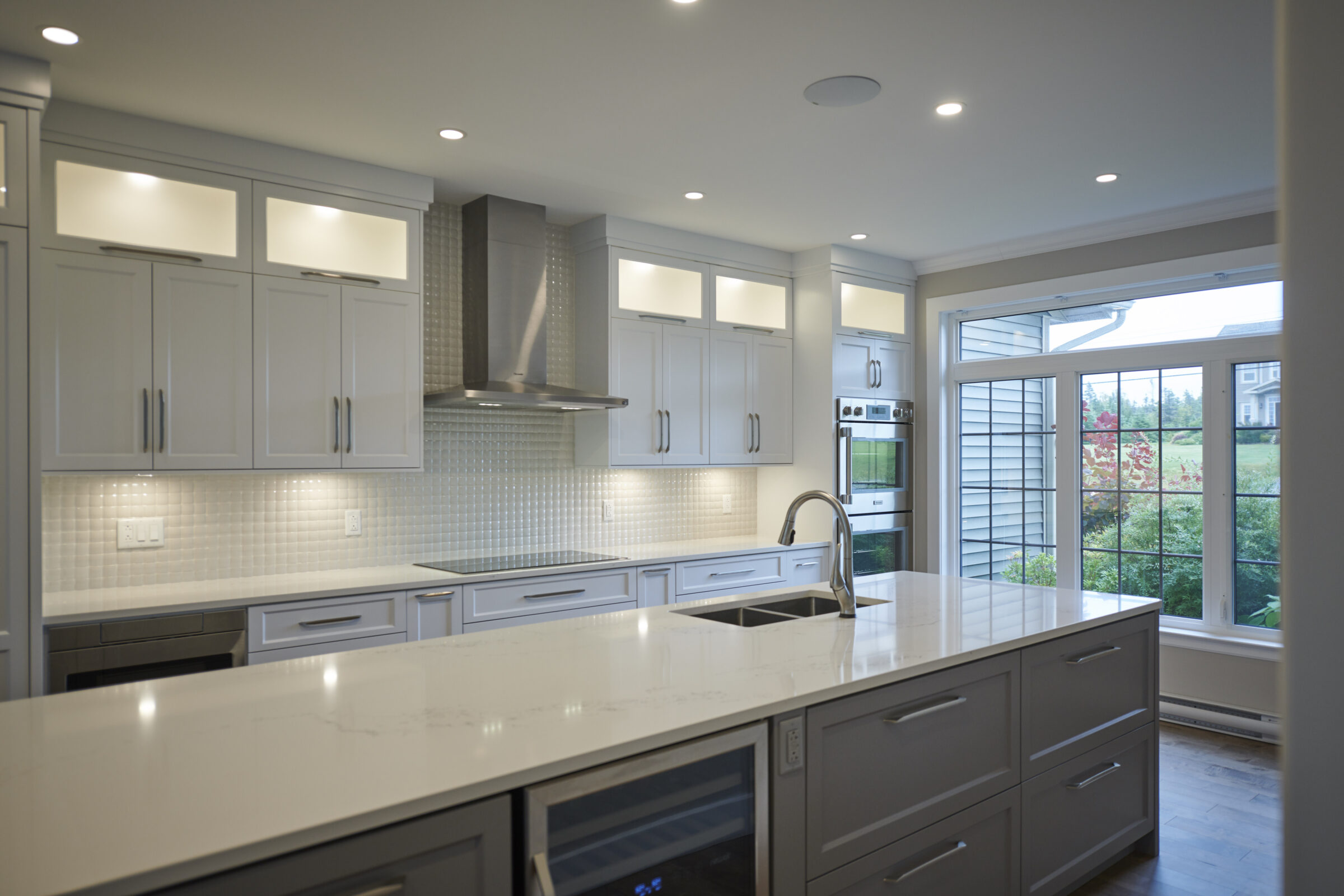 A modern kitchen with white cabinets, stainless steel appliances, recessed lighting, and a large island overlooking a window with a view outdoors.