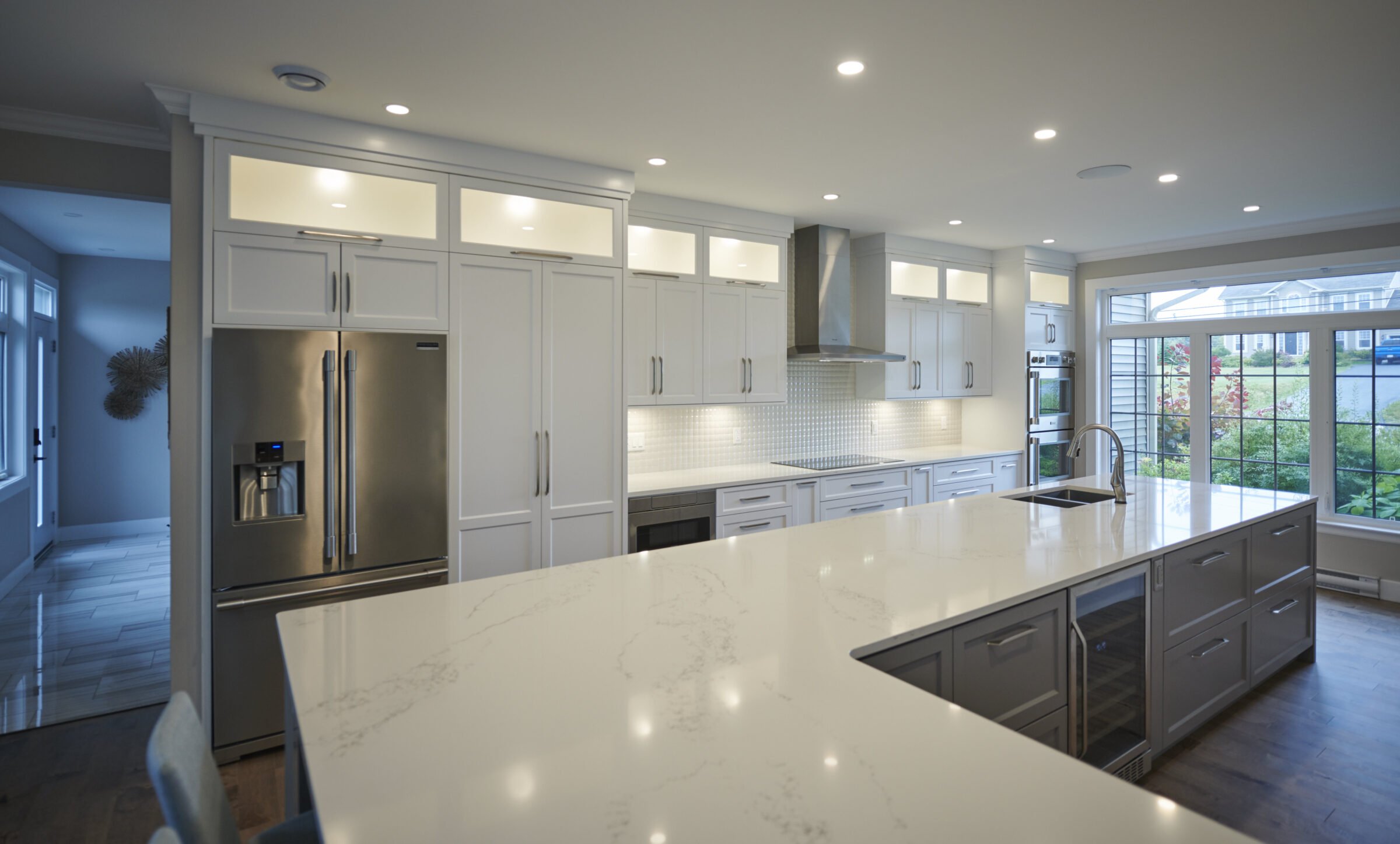 A modern kitchen with white cabinets, stainless steel appliances, a large island with a marble countertop, and an open window with a view outside.