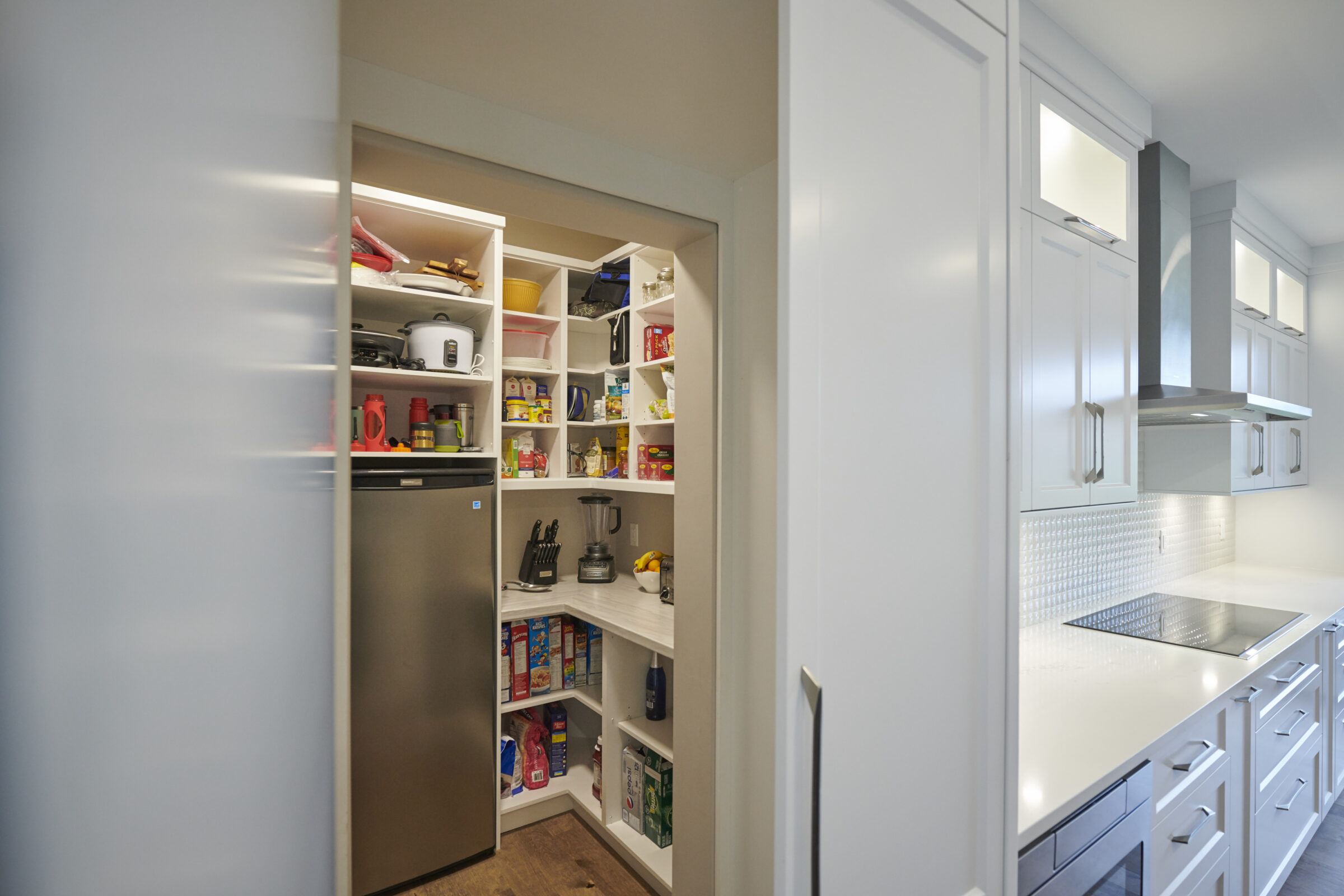 Modern kitchen with white cabinets and stainless steel appliances. An open pantry is full of organized food items, kitchenware, and small appliances.