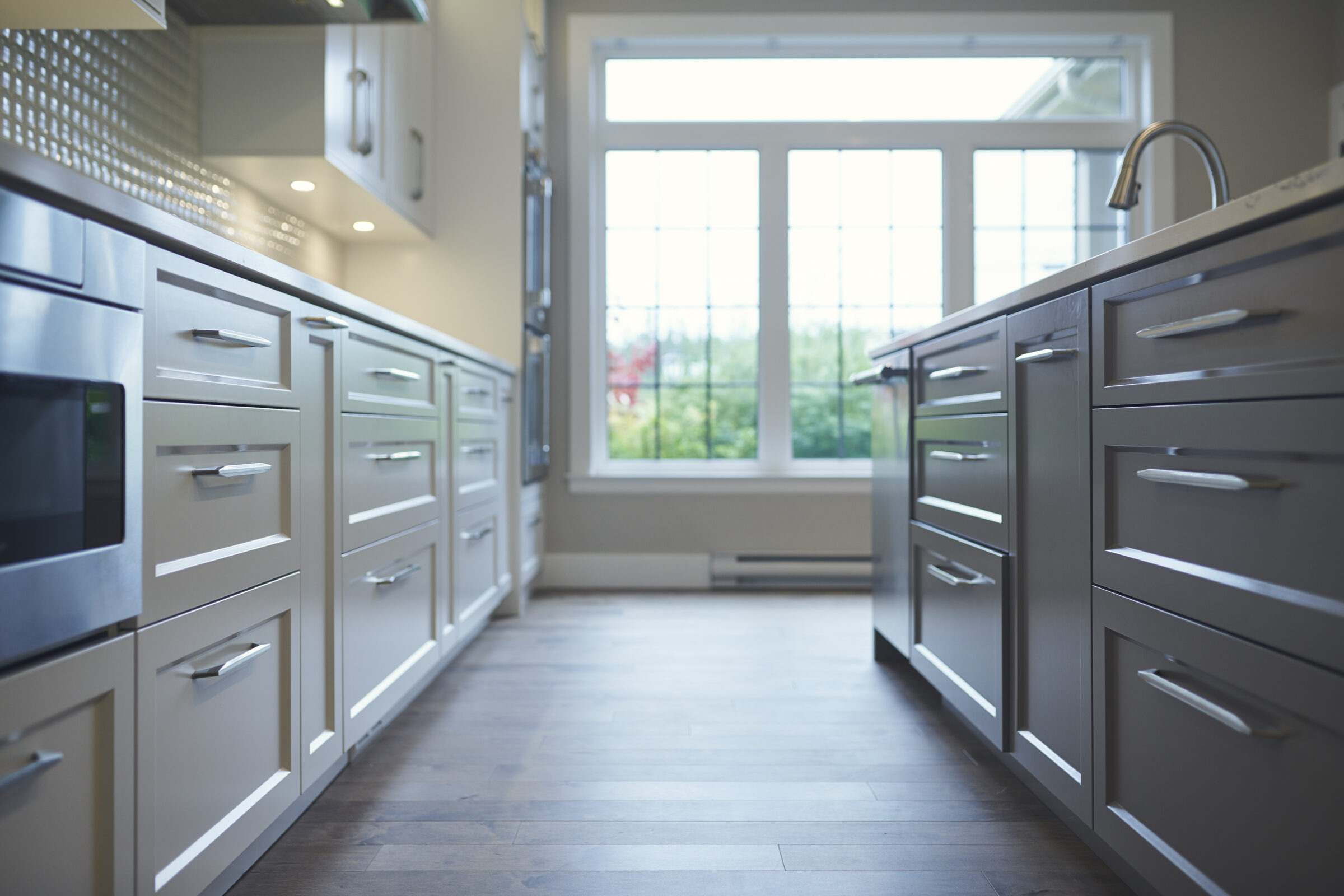 A modern kitchen interior with stainless steel appliances, white cabinetry, and hardwood floors. A bright window lets in natural light. The focus is soft.
