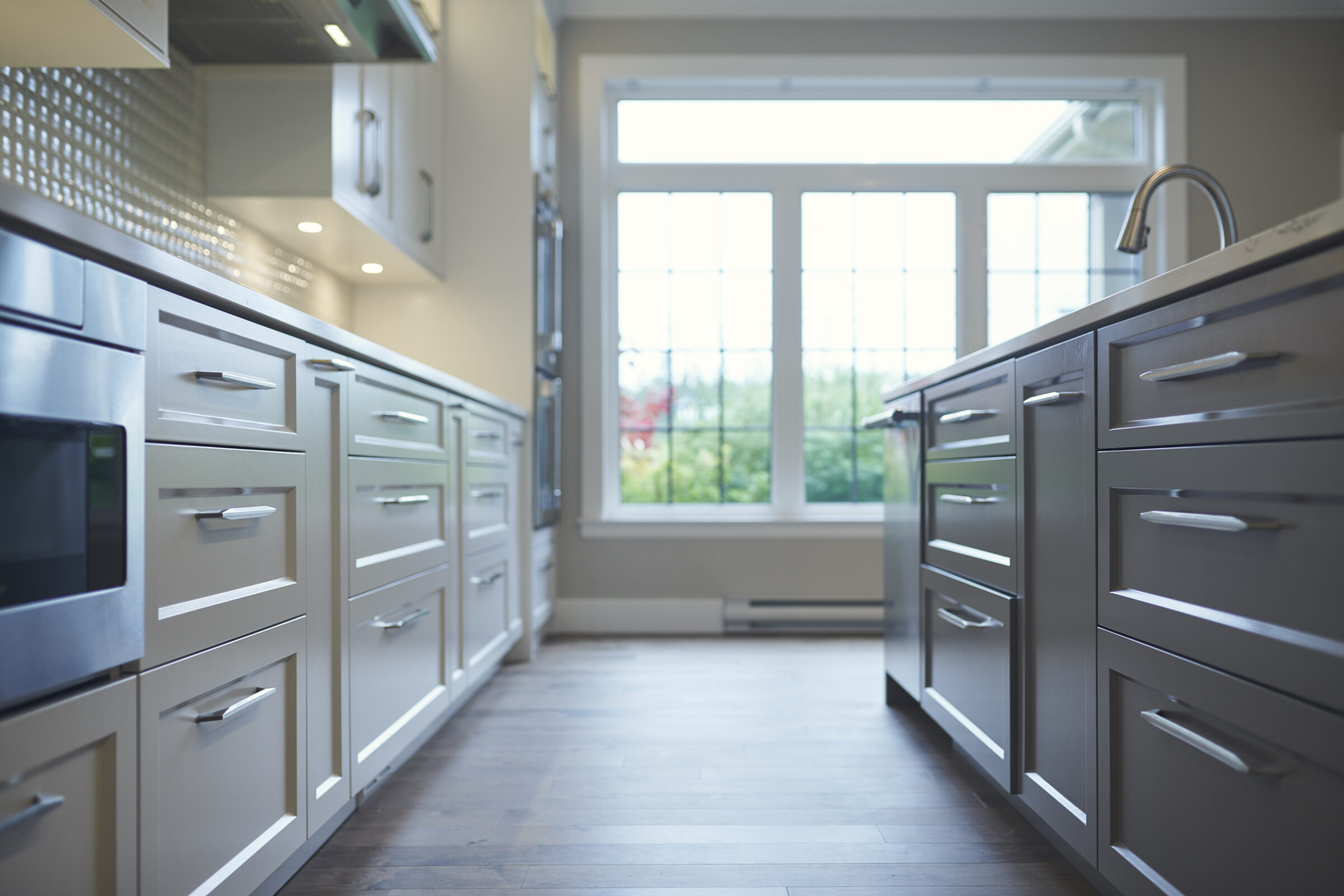 Modern kitchen interior with stainless steel appliances, white cabinets, dark wood floor, and a large window letting in natural light.