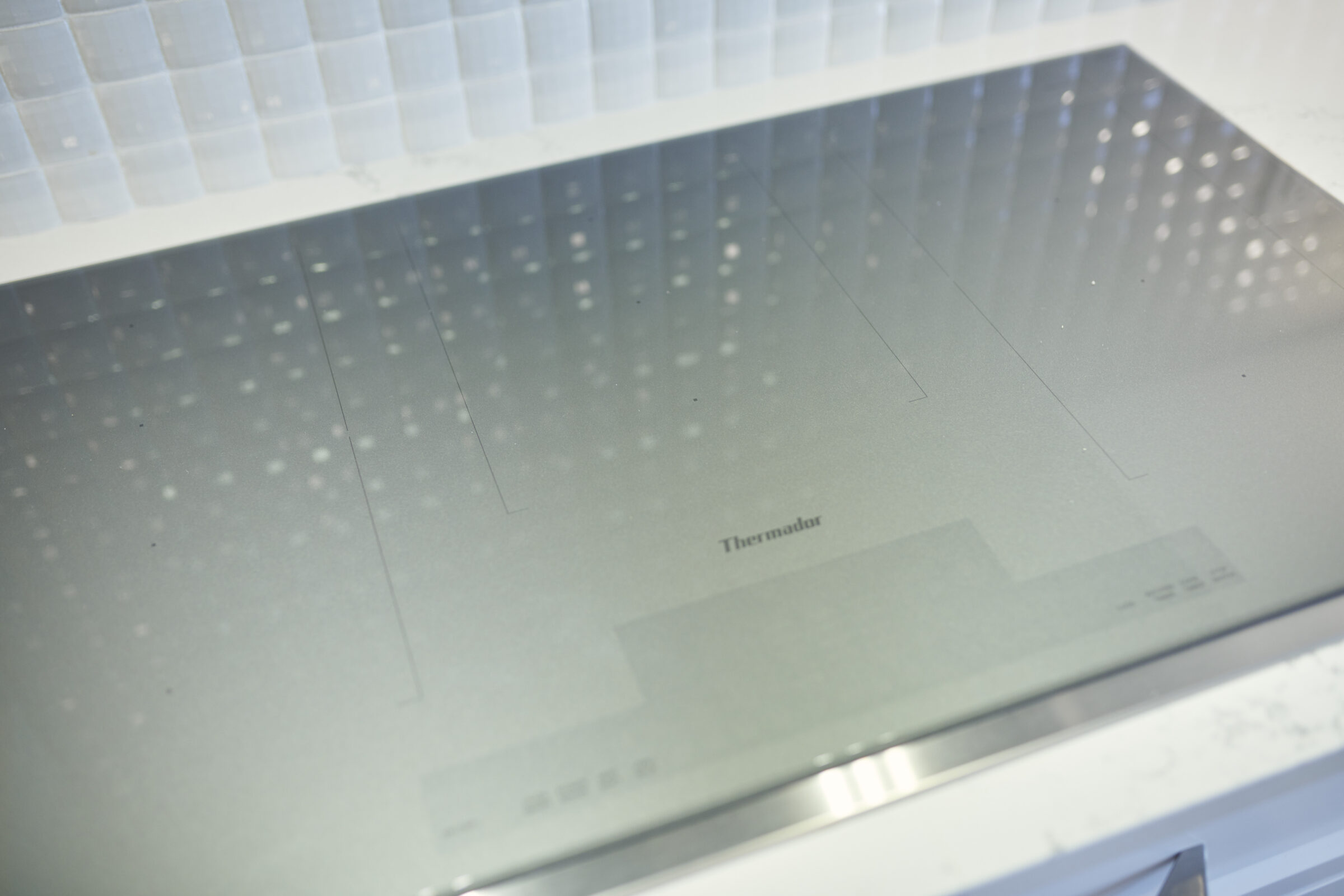 This image shows a modern induction cooktop with a sleek design, featuring touch controls and the brand Thermador visible. It's installed in a kitchen.