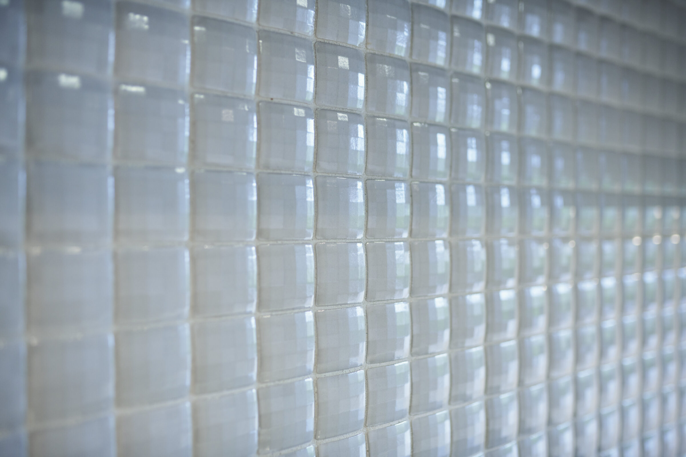 This image shows a wall covered in small, square, light-colored tiles with a glossy finish, arranged neatly and reflecting some ambient light.