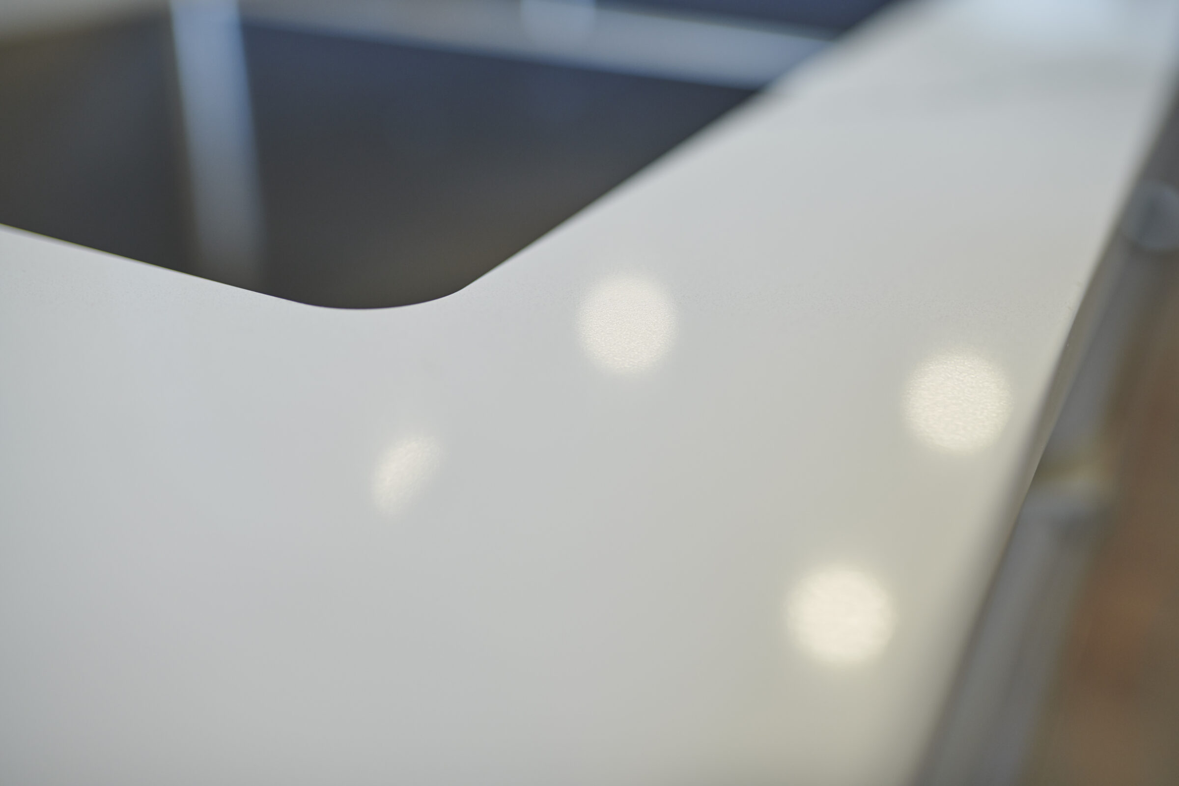 This is a close-up image of a white, curved surface, likely a countertop, with a blurred background and soft light reflections on the surface.