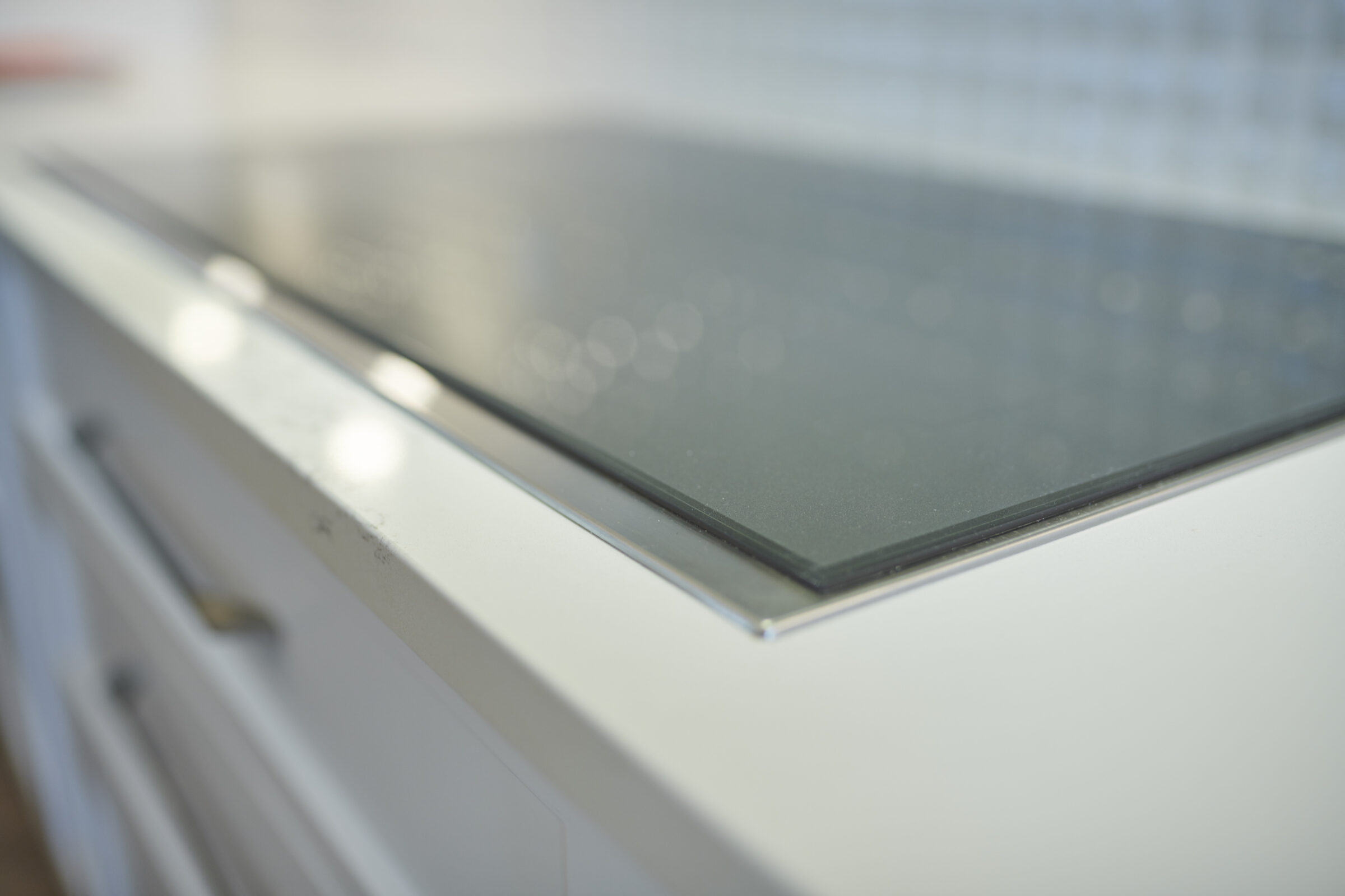 The image shows a close-up of a dusty white kitchen cabinet with a modern black glass cooktop, featuring a blurred background, emphasizing cleanliness.
