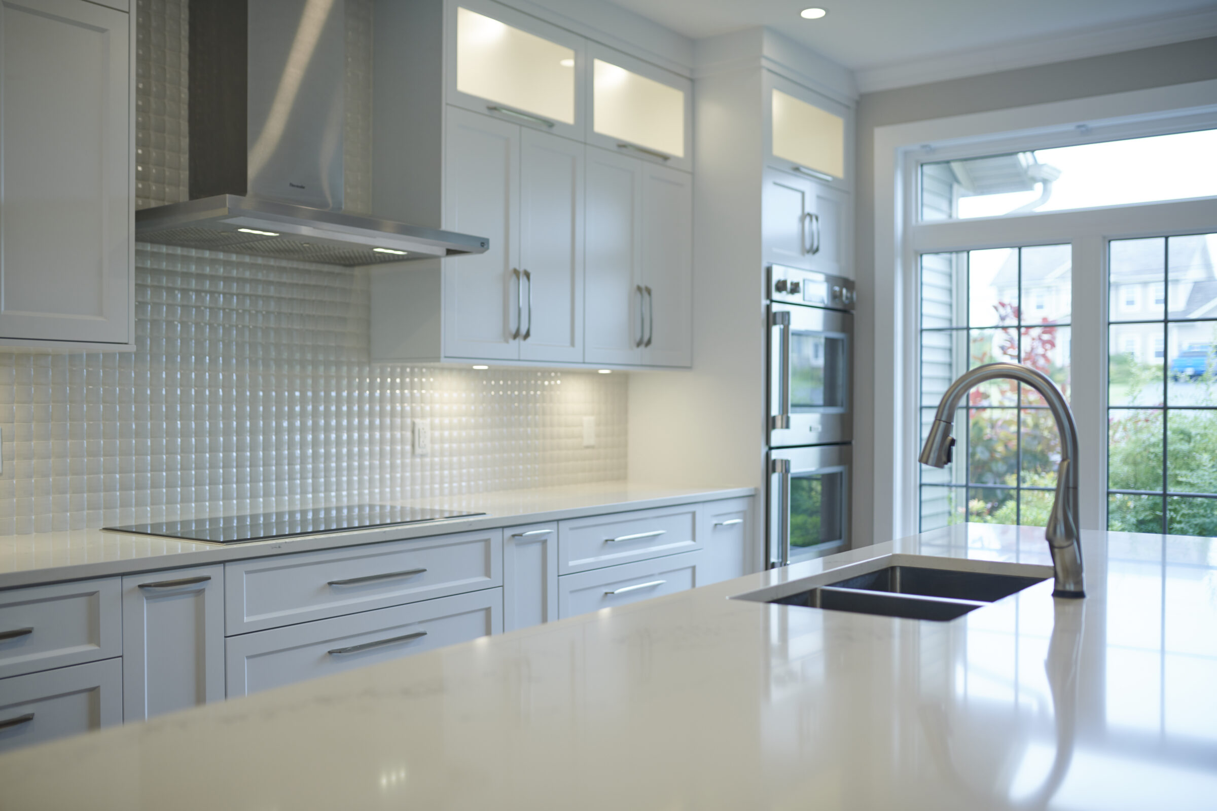 Modern kitchen interior featuring white cabinets, stainless steel appliances, a glossy backsplash, and a marble countertop with a deep sink and faucet.