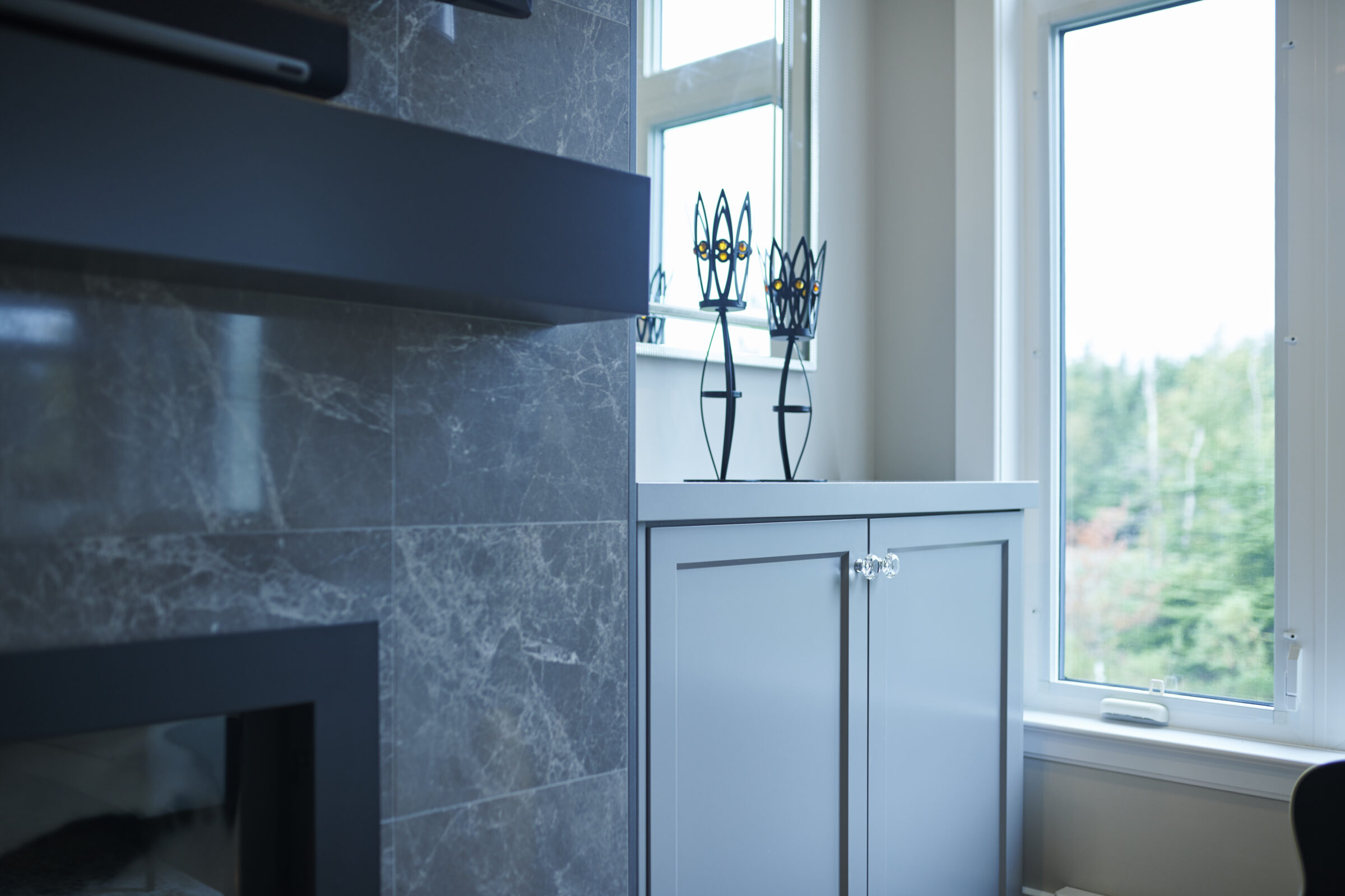 This is a modern room with marble walls, a gray cabinet, decorative metal vases on top, and a window looking out to greenery.