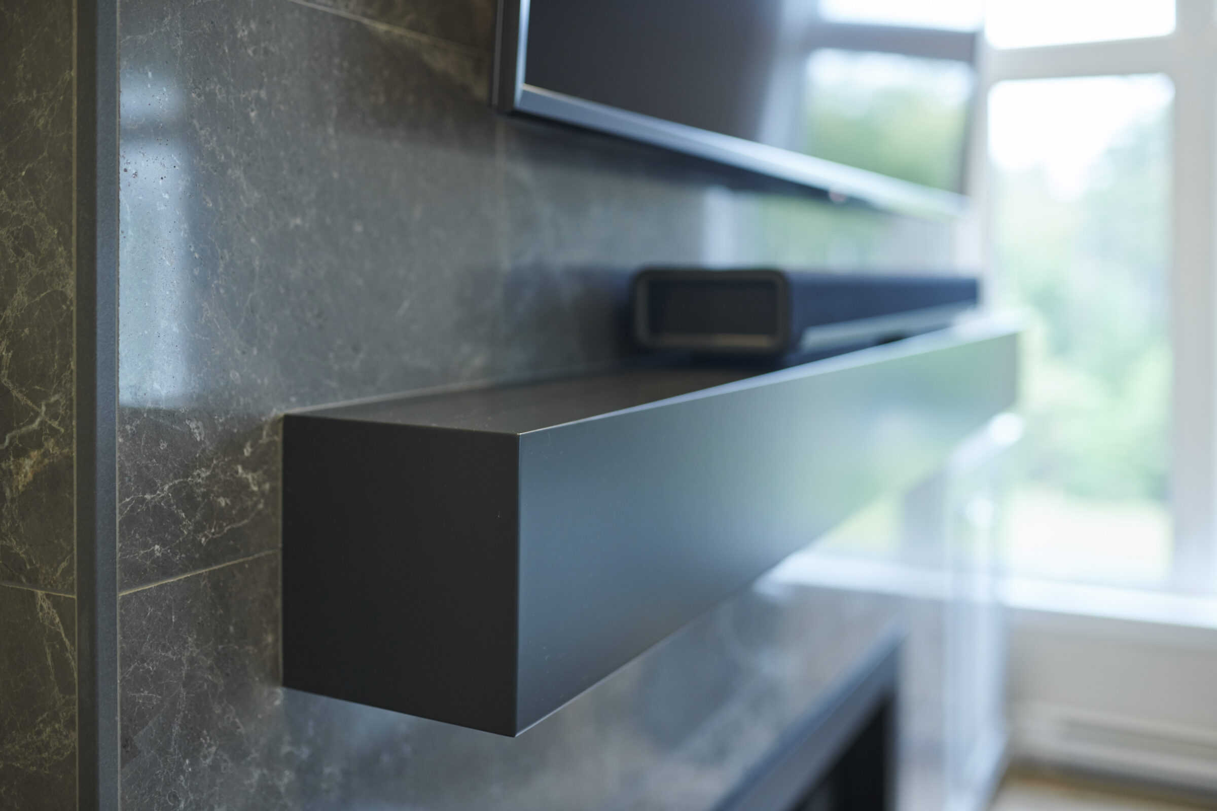 This image shows a modern kitchen with dark, floating shelves against a marble backsplash. The focus is shallow, leaving the background blurred.
