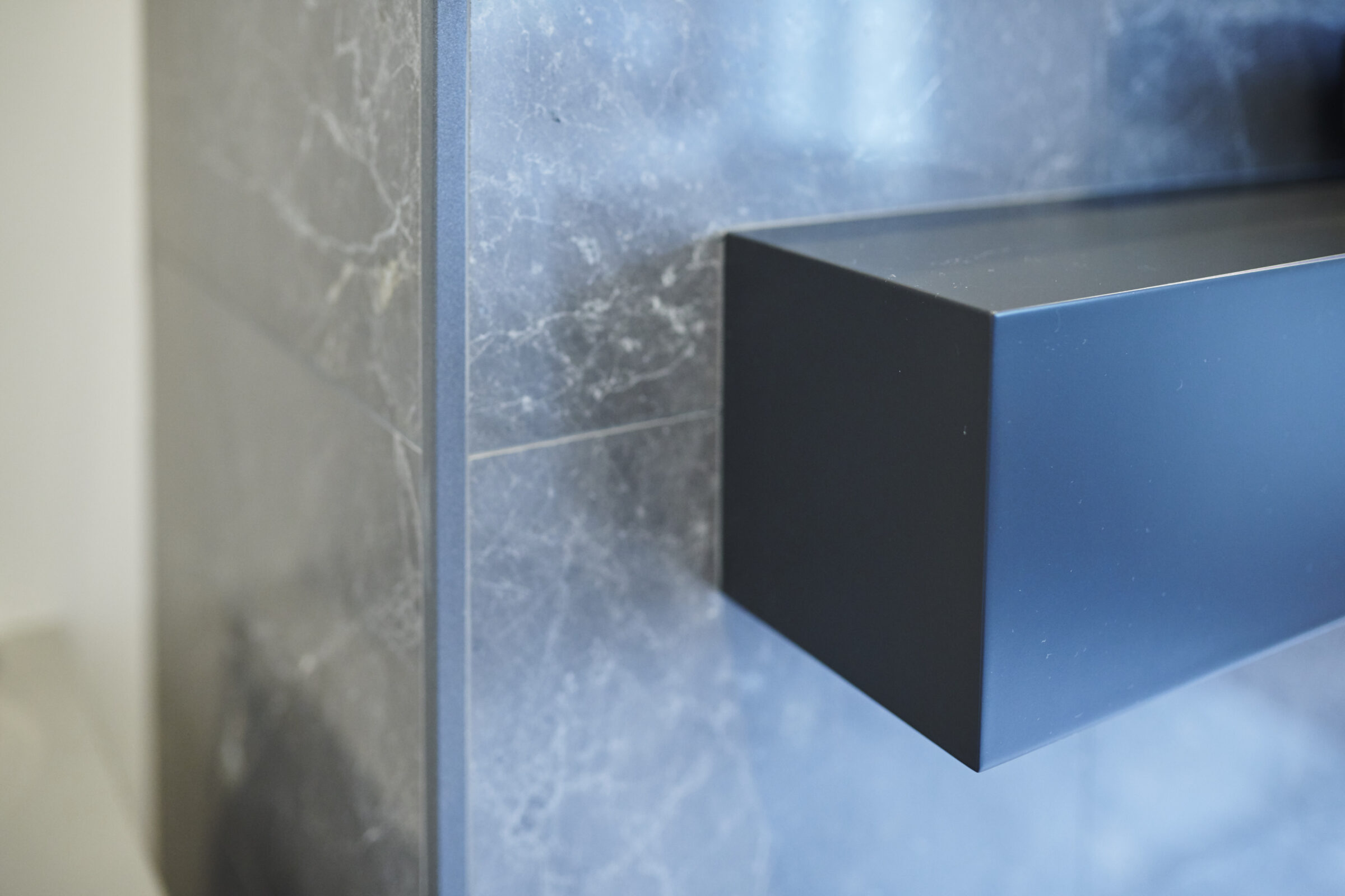 A sleek black floating shelf against a textured marble blue wall, showing a modern, minimalist design with a focus on clean lines and simplicity.