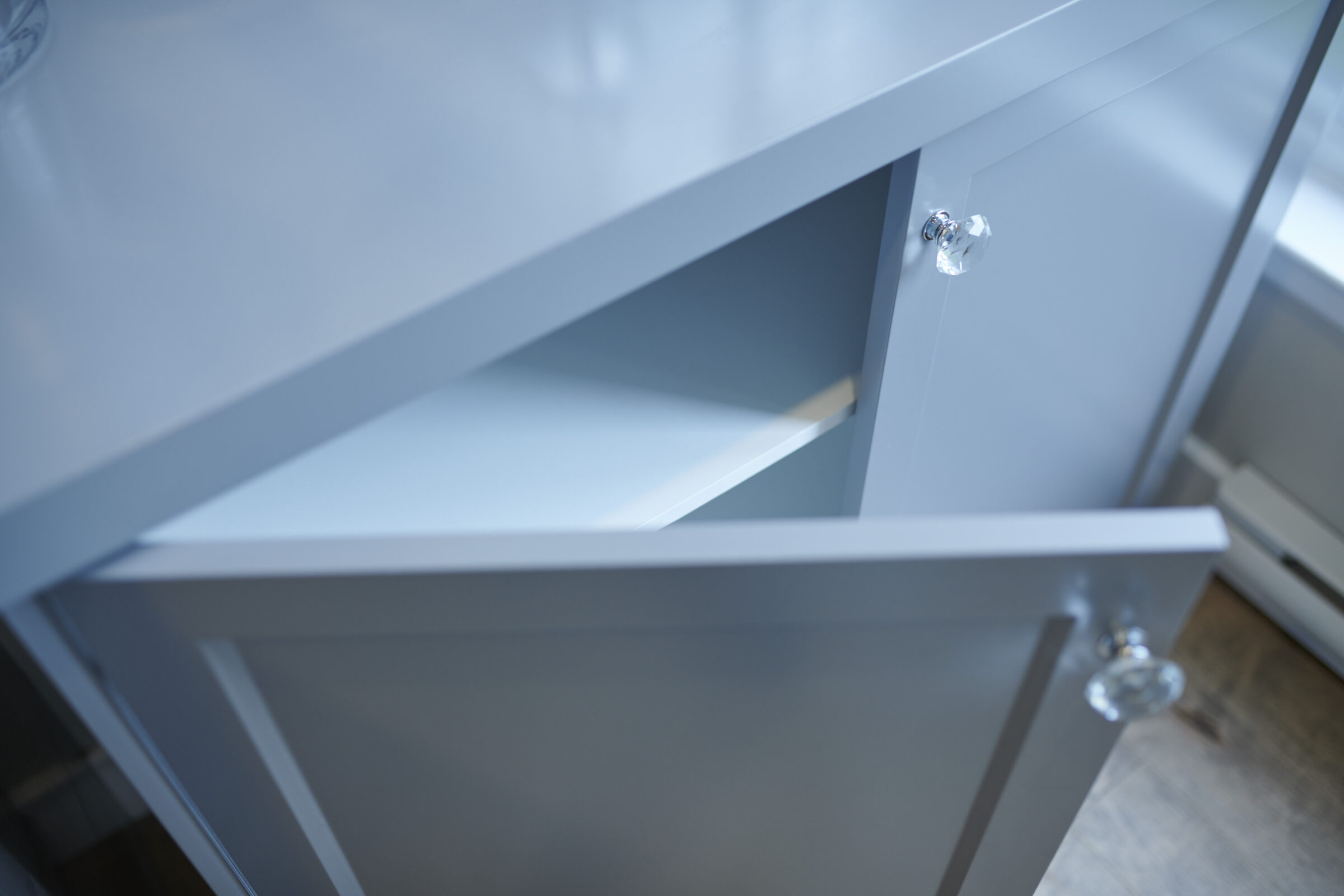 A close-up view of an open, empty, light-colored drawer with a clear knob, part of a modern kitchen or storage cabinet.