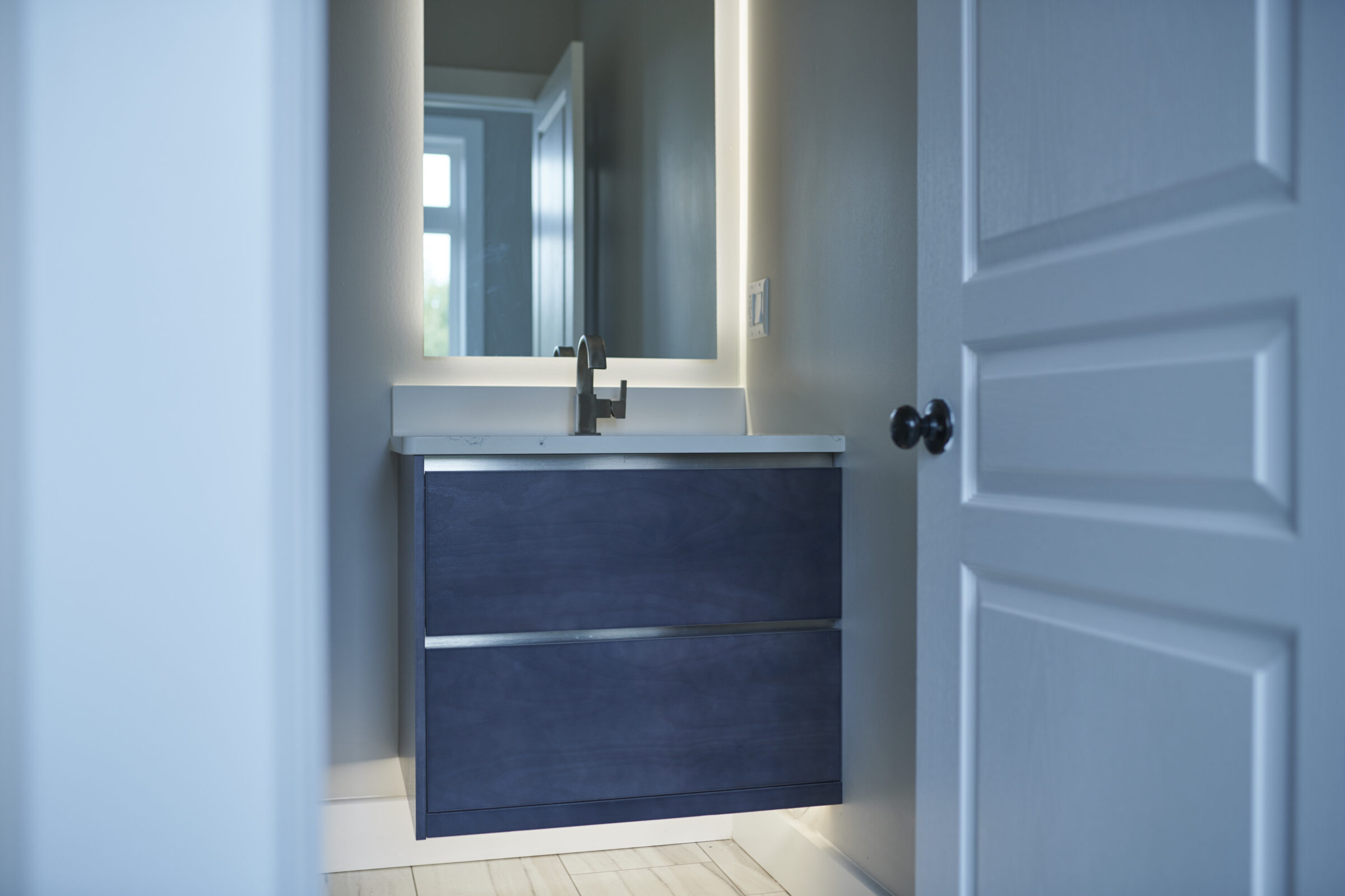 A modern bathroom vanity with a sink and mirror is visible through an open door, illuminated by natural and artificial light in a clean space.