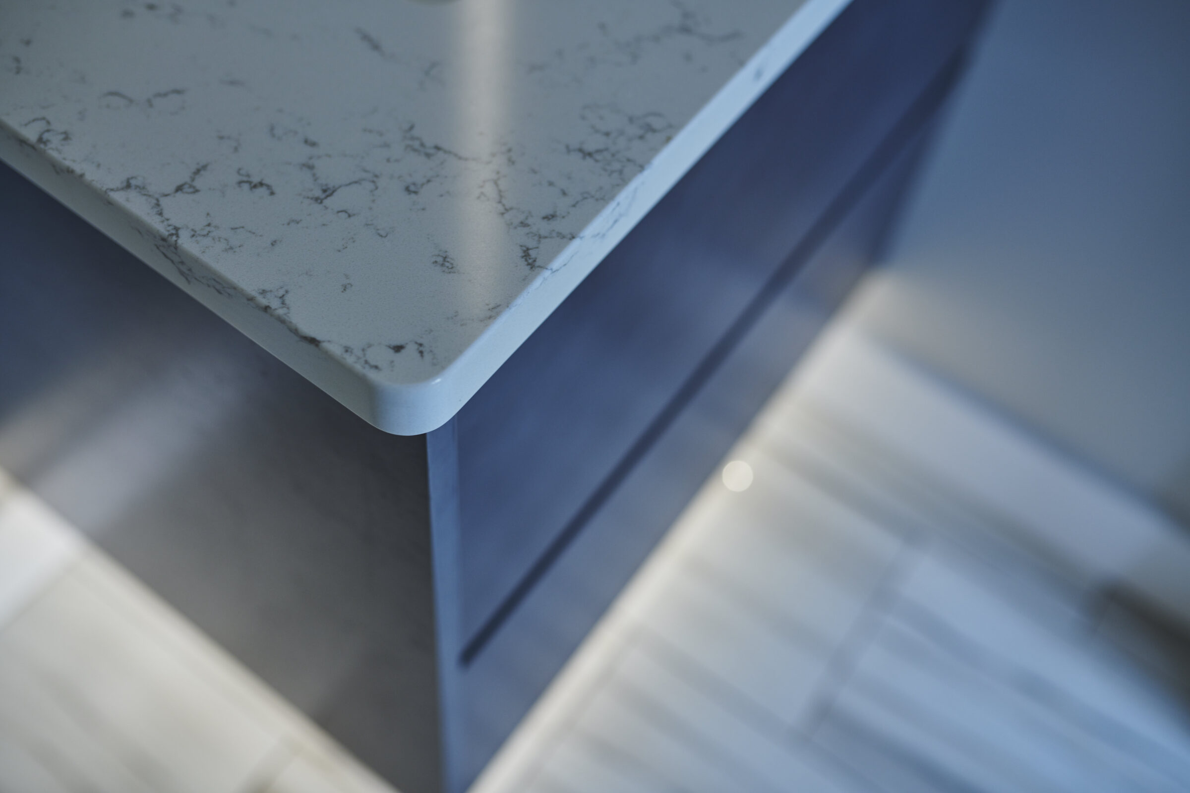 The image showcases a close-up angle of a marble countertop with a round edge, above a navy blue cabinet, against a blurry background.
