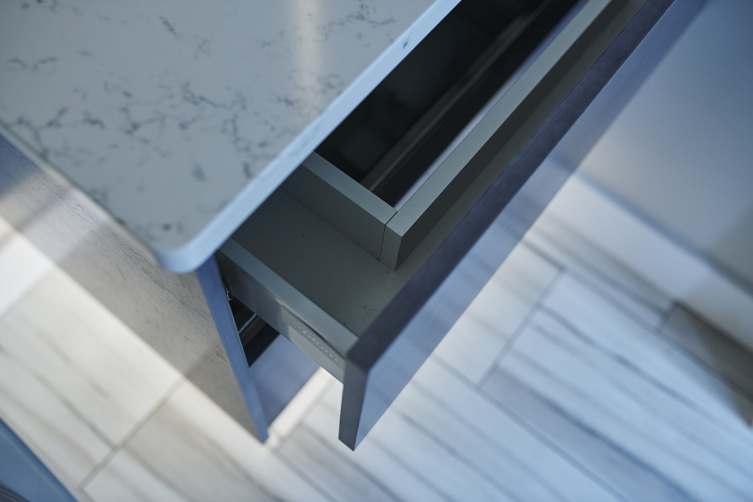 The image shows a close-up, angled view of a modern kitchen with a focus on a marble countertop and the corner of an open drawer.