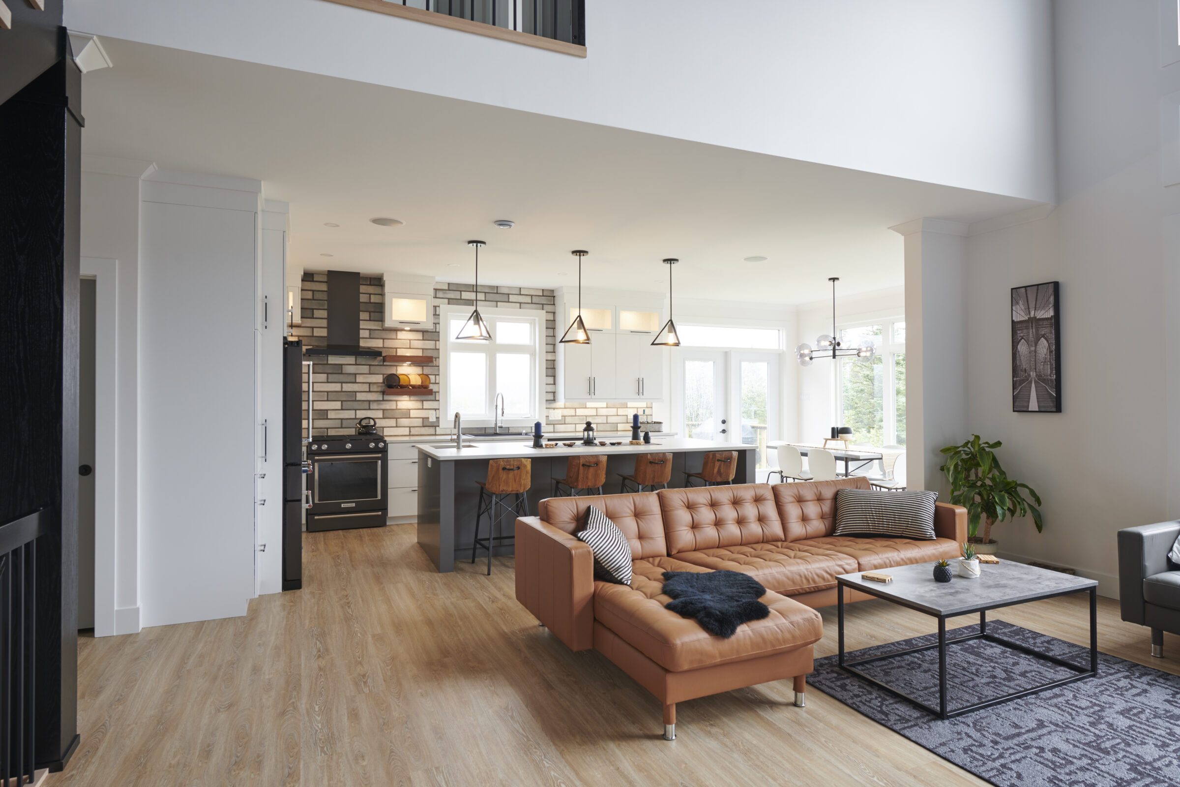 Open-plan living space with kitchen, dining area, and lounge; leather couch, wood flooring, pendant lights, modern appliances, and neutral tones.