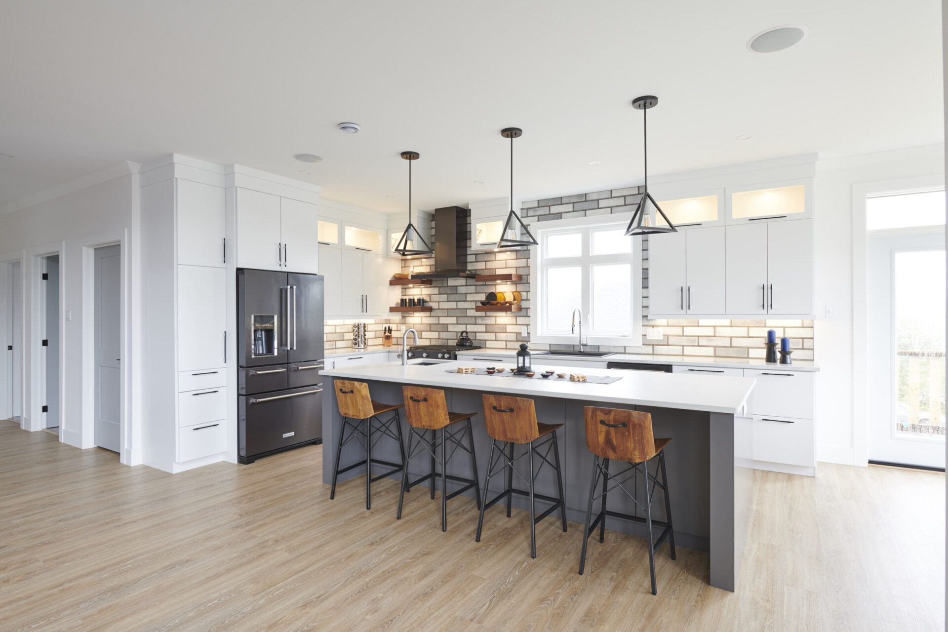 Modern kitchen interior with a center island, pendant lights, wooden stools, stainless steel appliances, white cabinets, and a light hardwood floor.