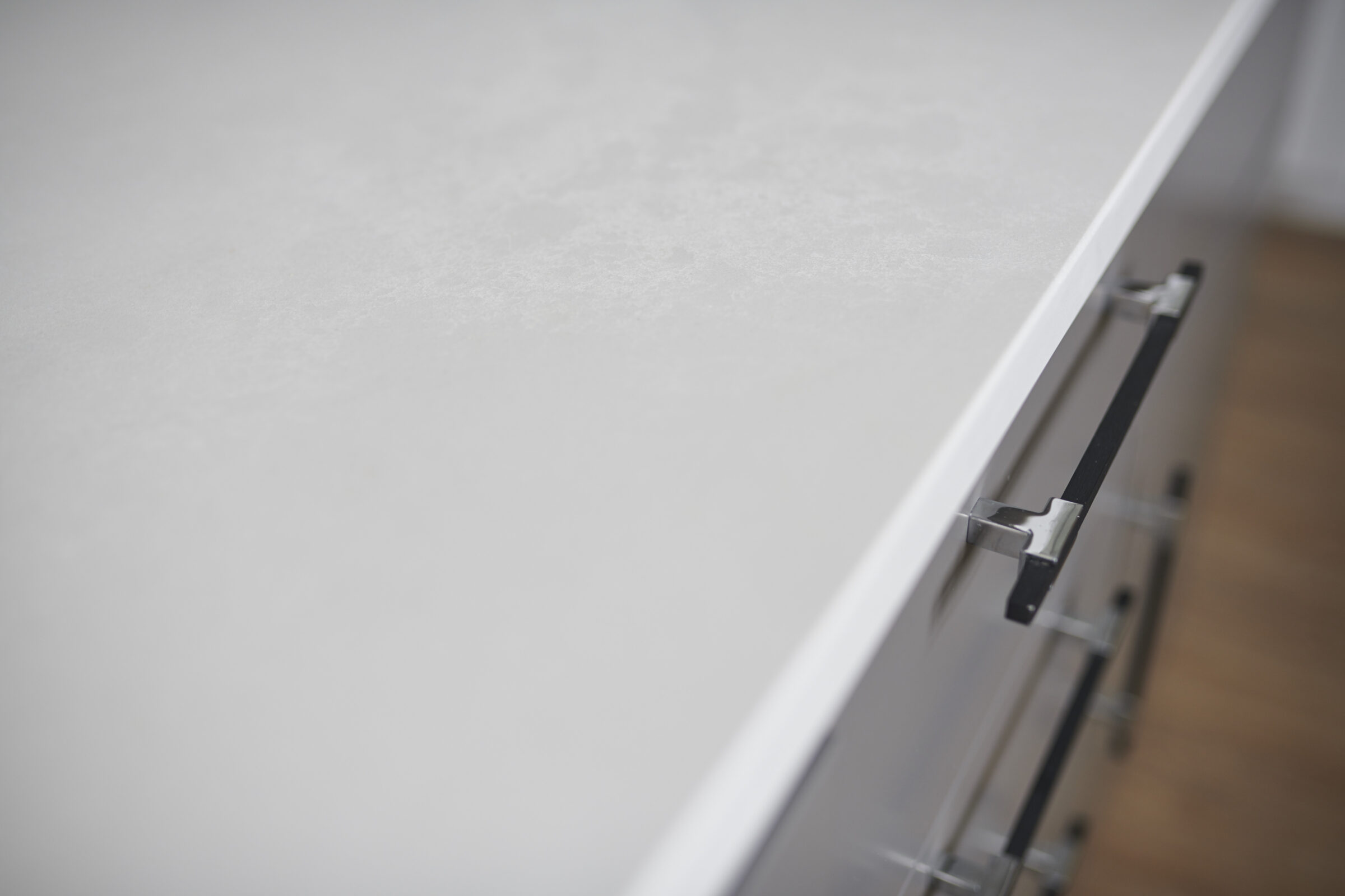 A close-up of a white countertop with a slight texture, featuring a metal drawer handle, blurred background, minimalist, clean, and modern design.