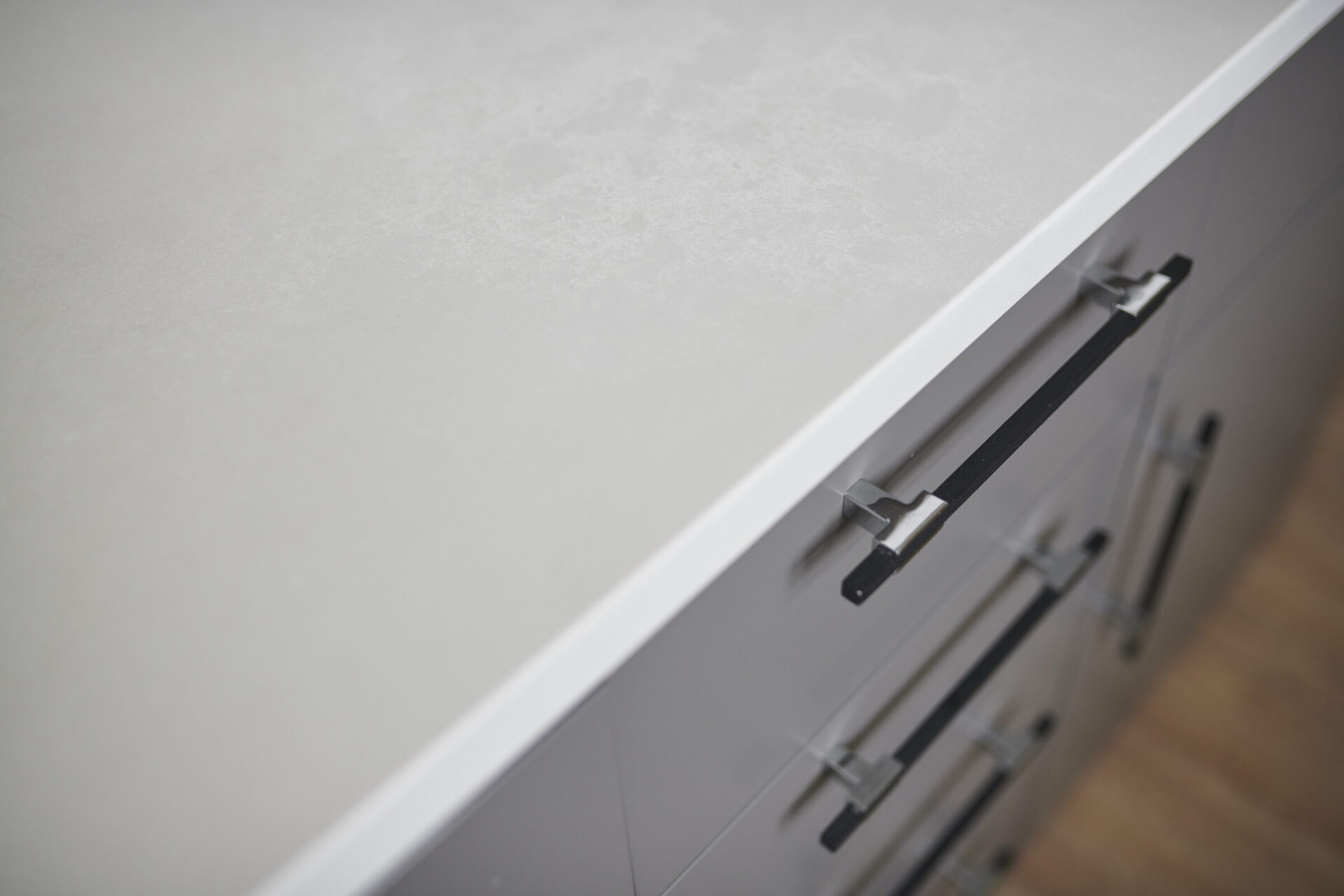 This image shows a close-up of a modern kitchen countertop with a shallow depth of field, focusing on a drawer handle among several cabinets.