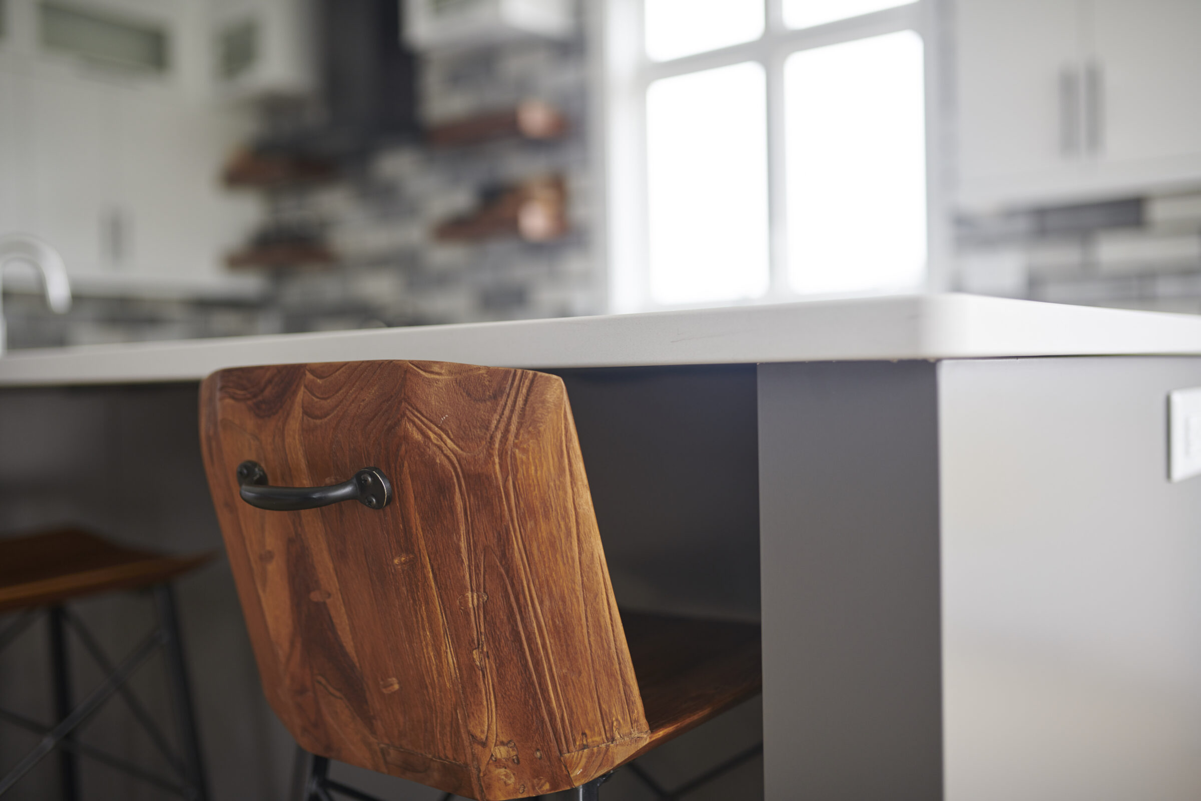A modern kitchen interior with a focus on a wooden drawer with a black handle, white countertop, and blurred background showing shelves.