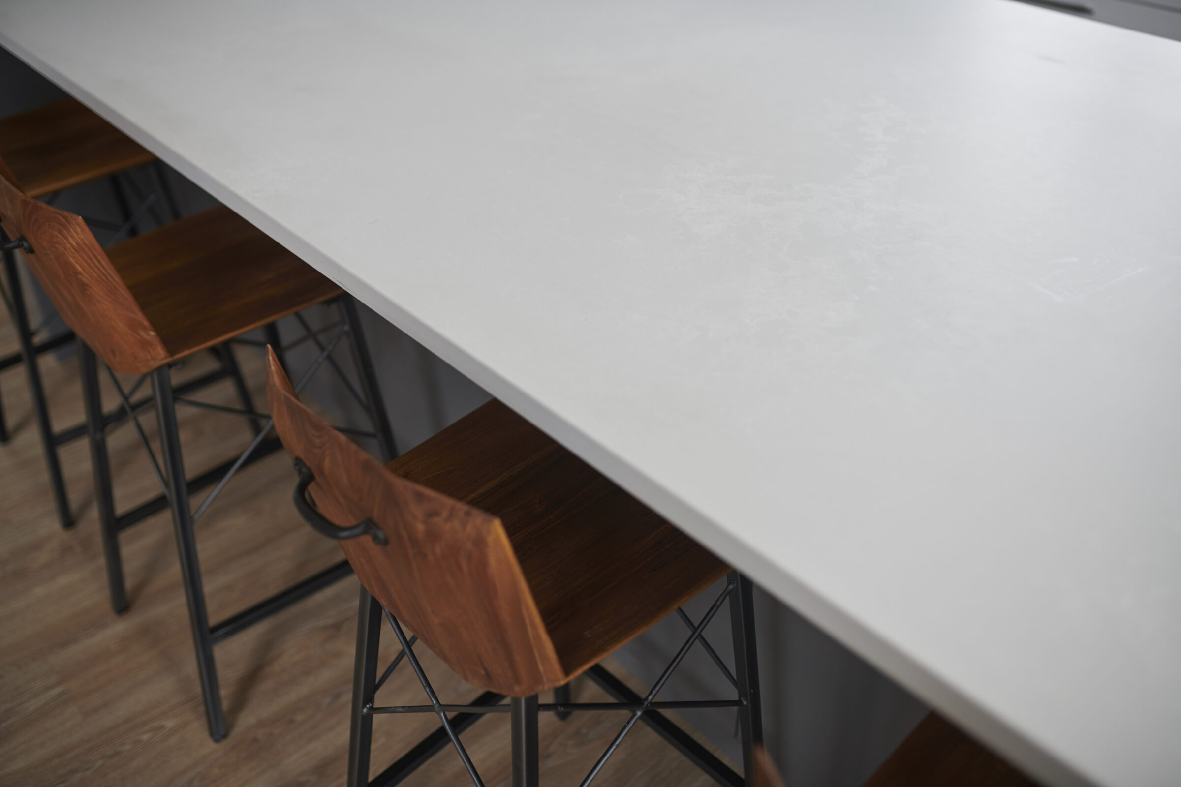 Modern interior with a long white tabletop and several wooden chairs with black metal legs arranged neatly on a laminate flooring.